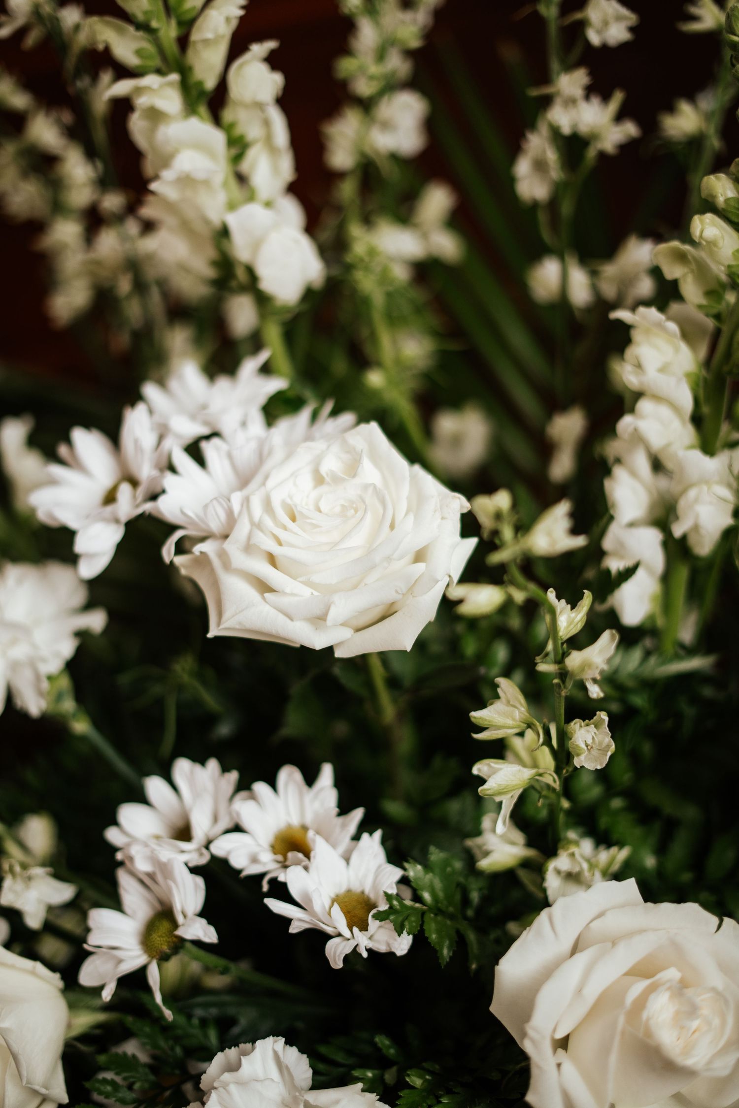 Close-up of elegant white wedding floral arrangement with roses, daisies, and delicate white blooms.