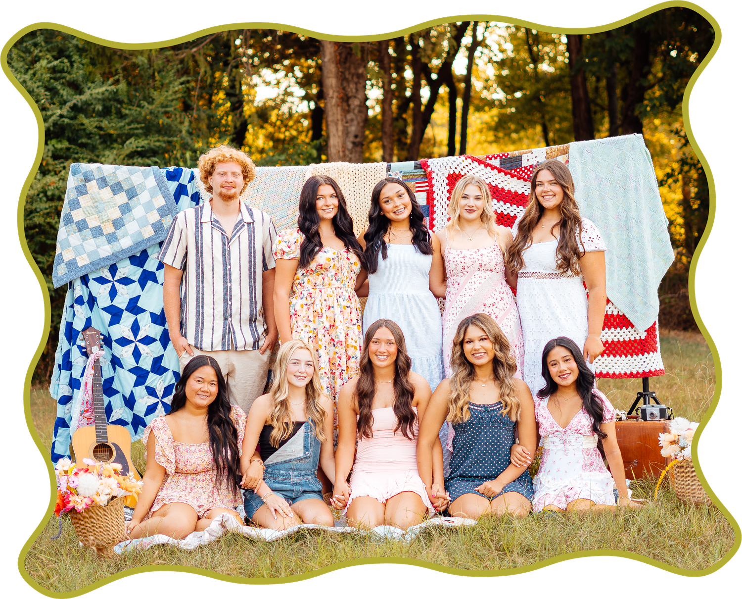 Group of smiling teens posing outdoors with colorful quilts displayed behind them.