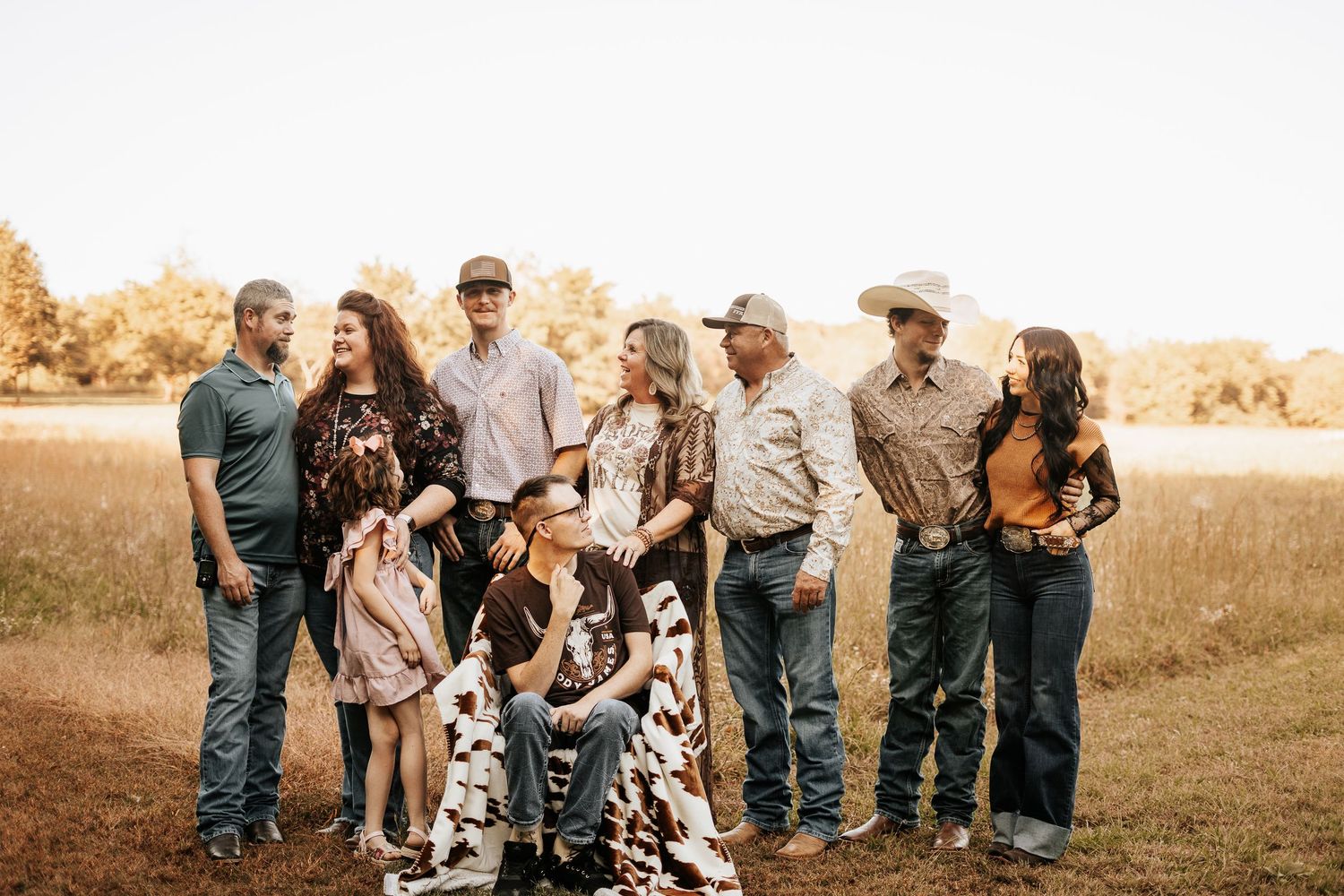 Large family group portrait in a golden field at sunset, wearing western attire and cowboy hats.