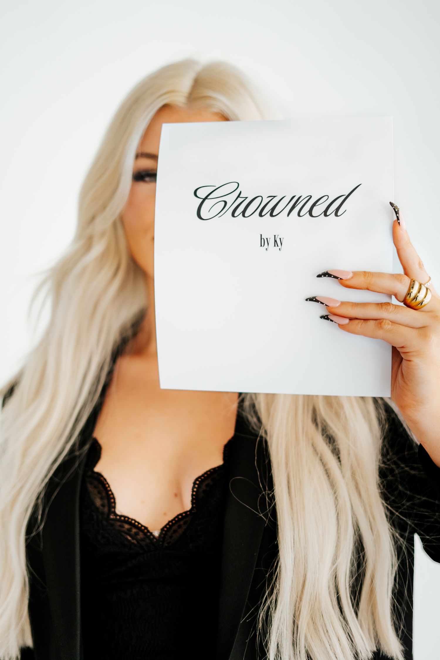 Blonde woman with long hair holding a Crowned by Ky book covering her face.