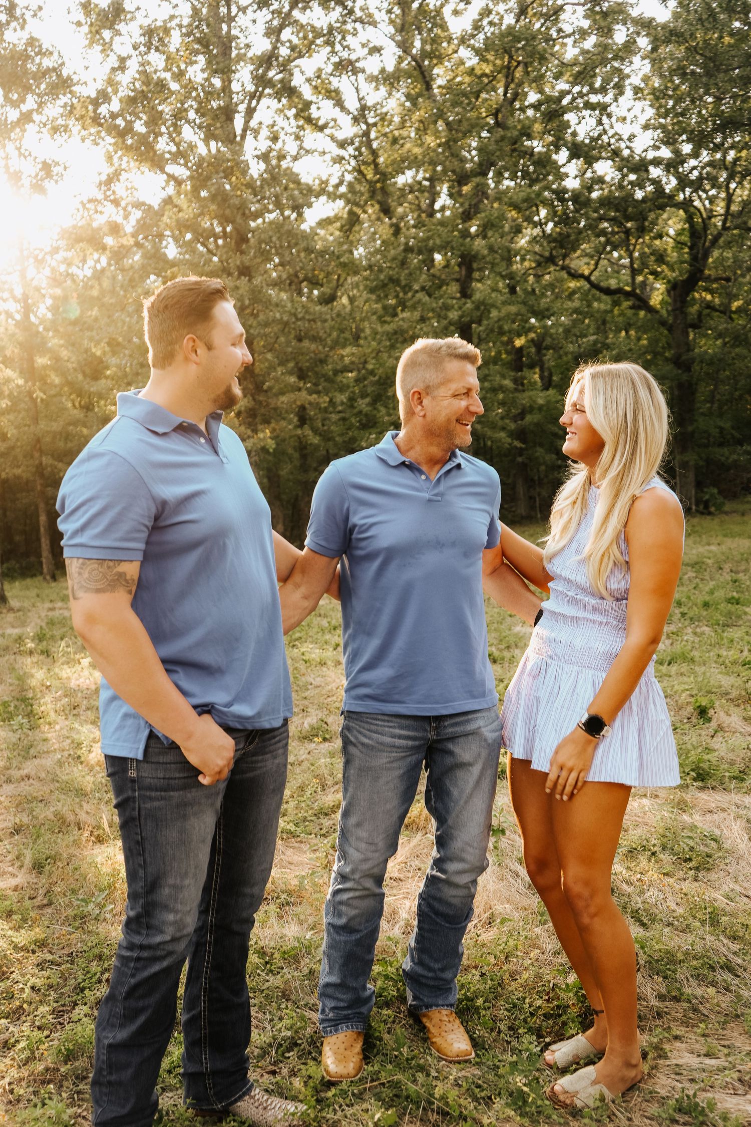 Two men and a woman in blue outfits laughing together in a sunlit field.