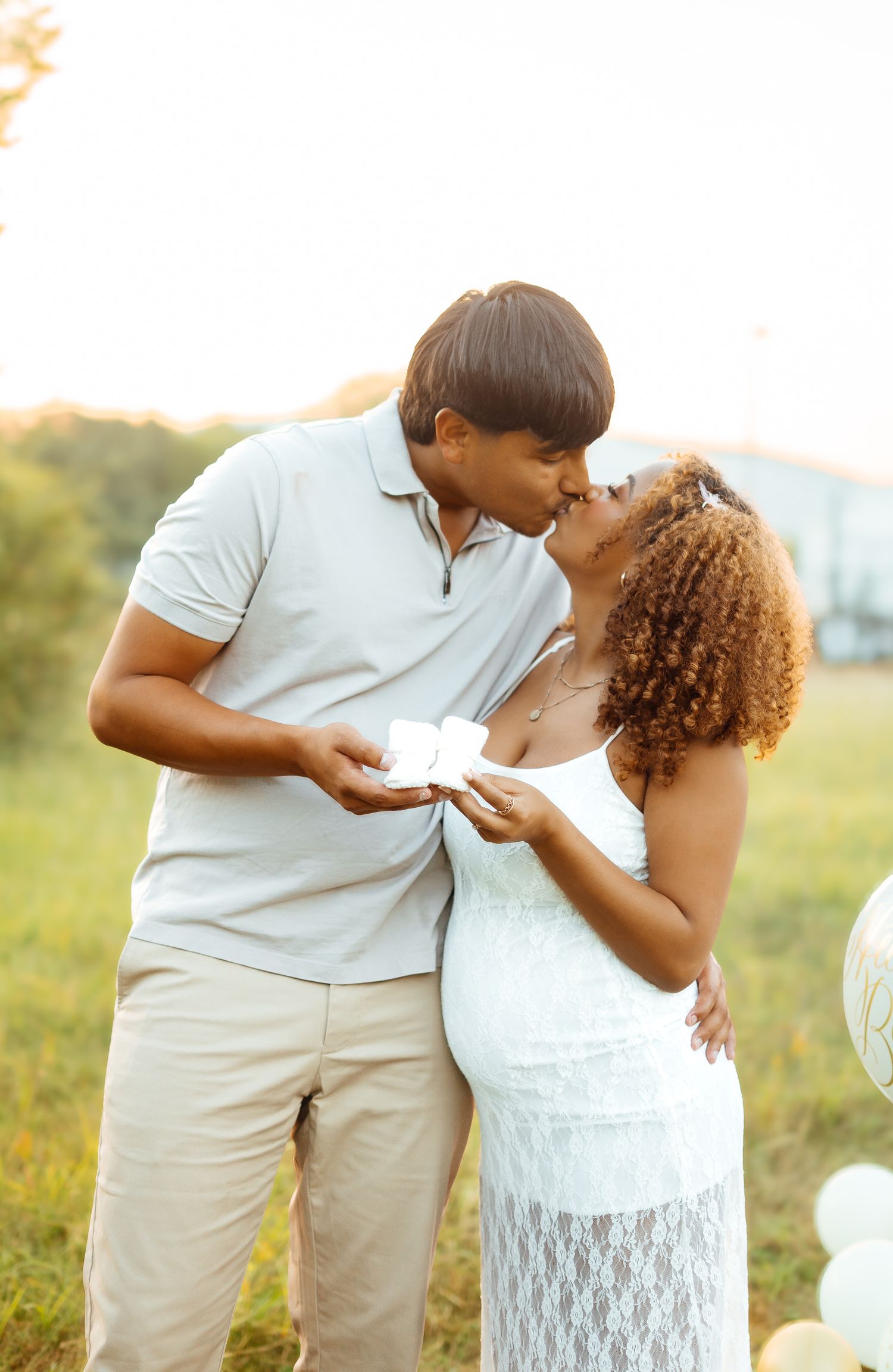 Couple kissing during outdoor gender reveal photoshoot at sunset in a field.