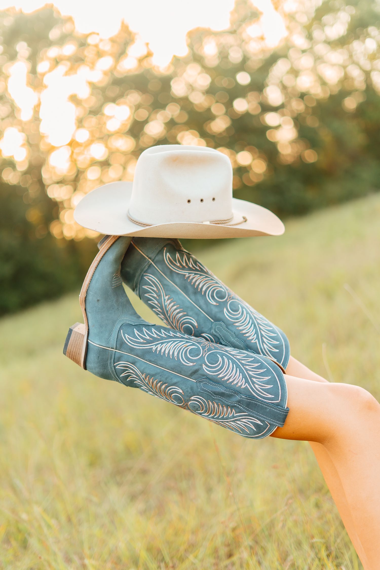 Blue embroidered cowboy boots held up with white cowboy hat balanced on top in field.