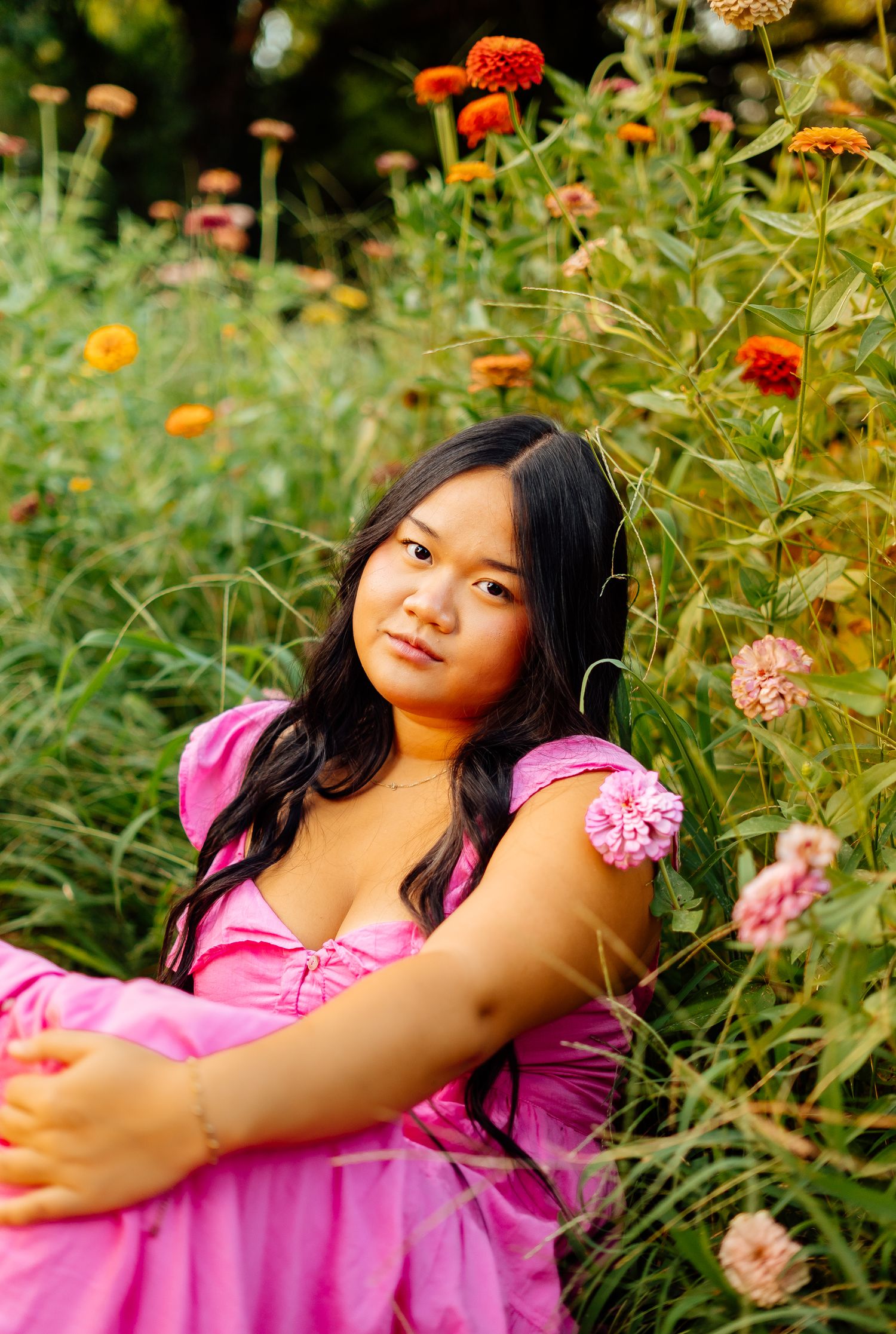 Young woman in a pink dress sits among colorful wildflowers in a lush garden setting.