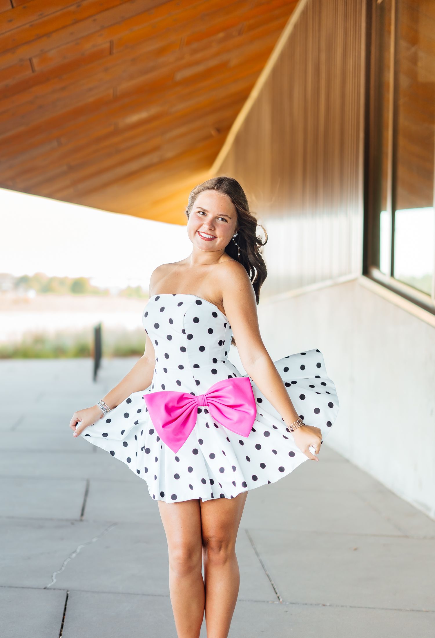 Young woman twirls in a strapless black and white polka dot dress with a large pink bow outdoors.