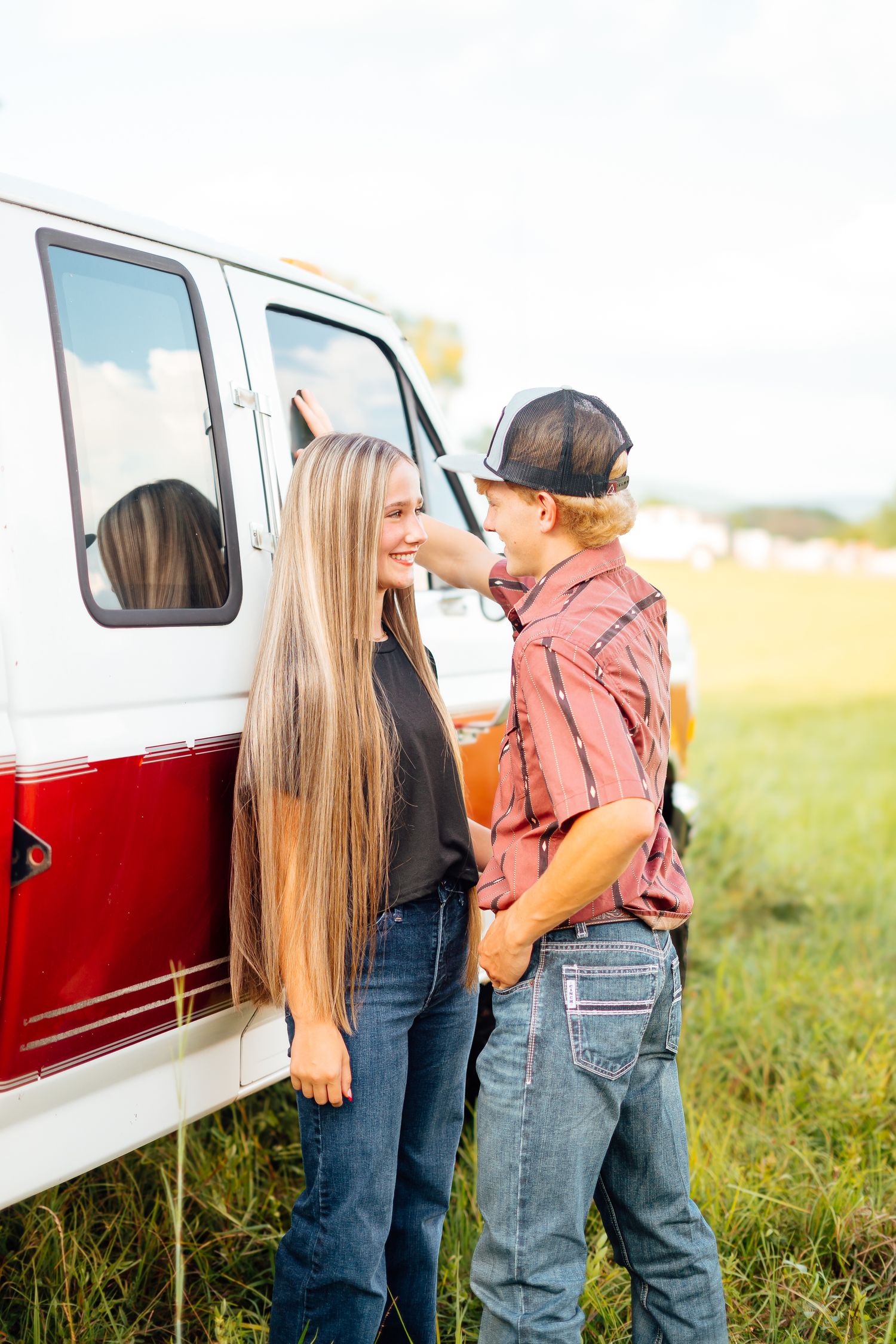 Couple sharing a tender moment beside a vintage red and white truck in an open field at golden hour.