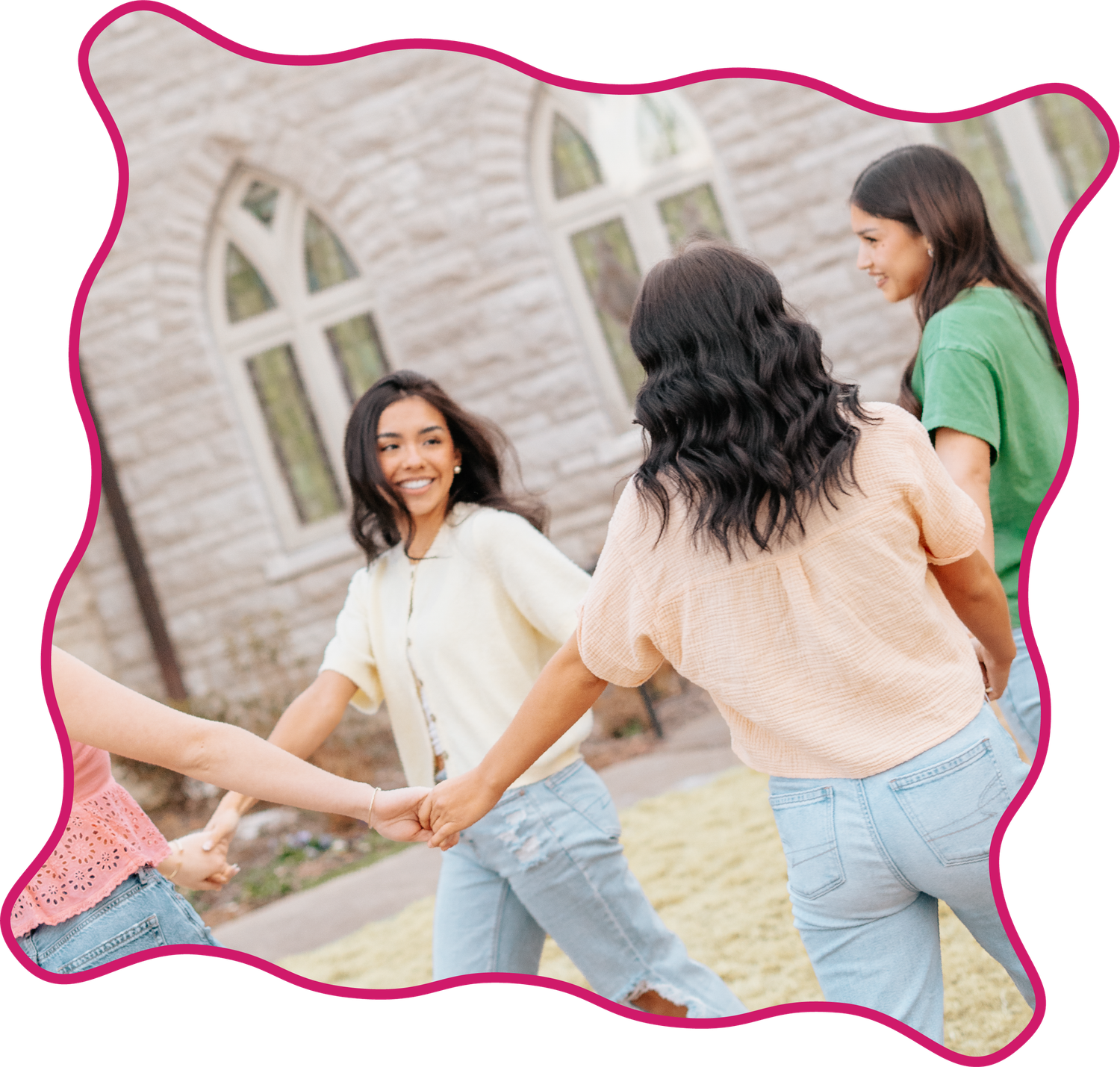 Teen girls laughing and holding hands in circle outside stone building.