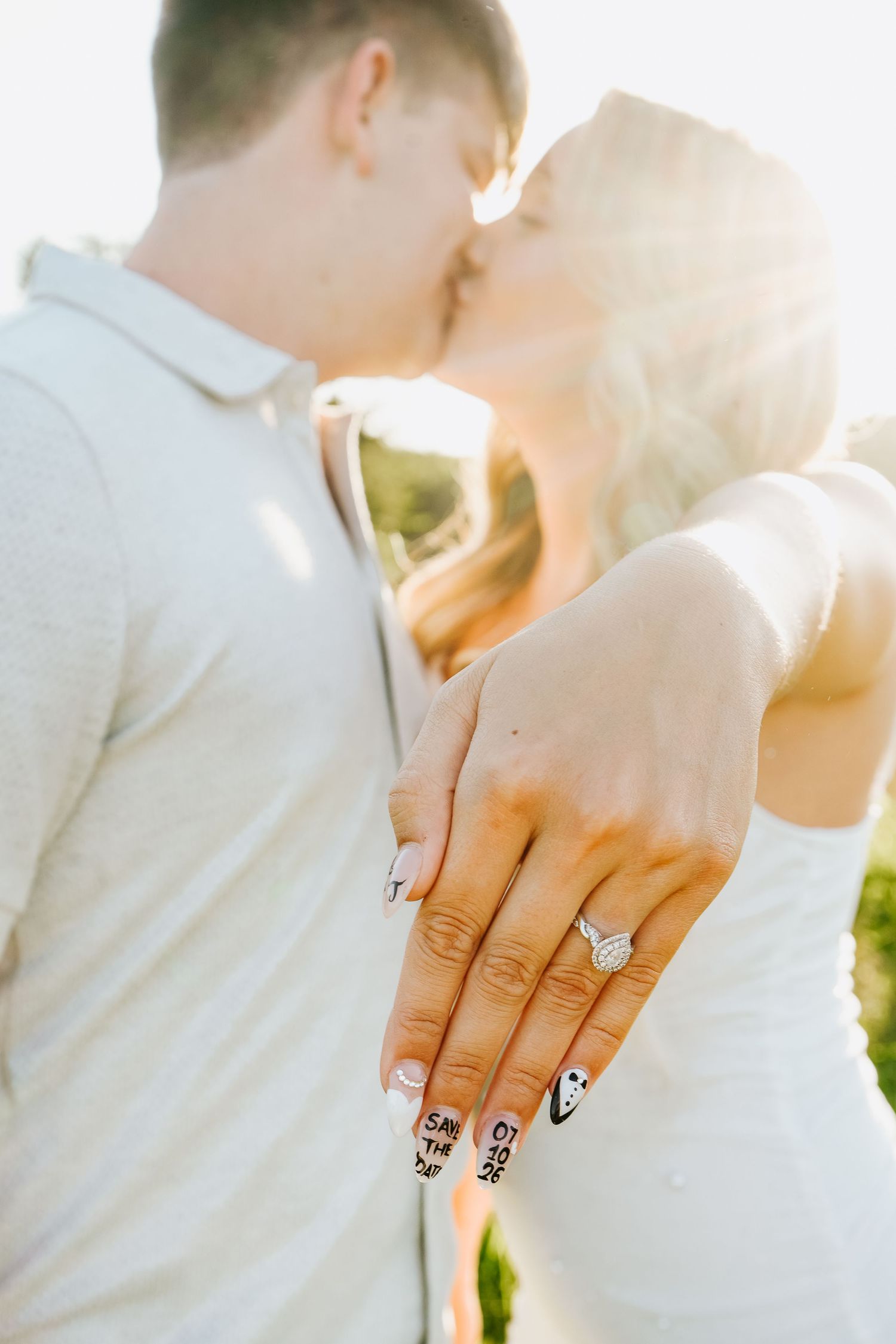 Couple kissing at sunset while showing off engagement ring with save the date nail art.