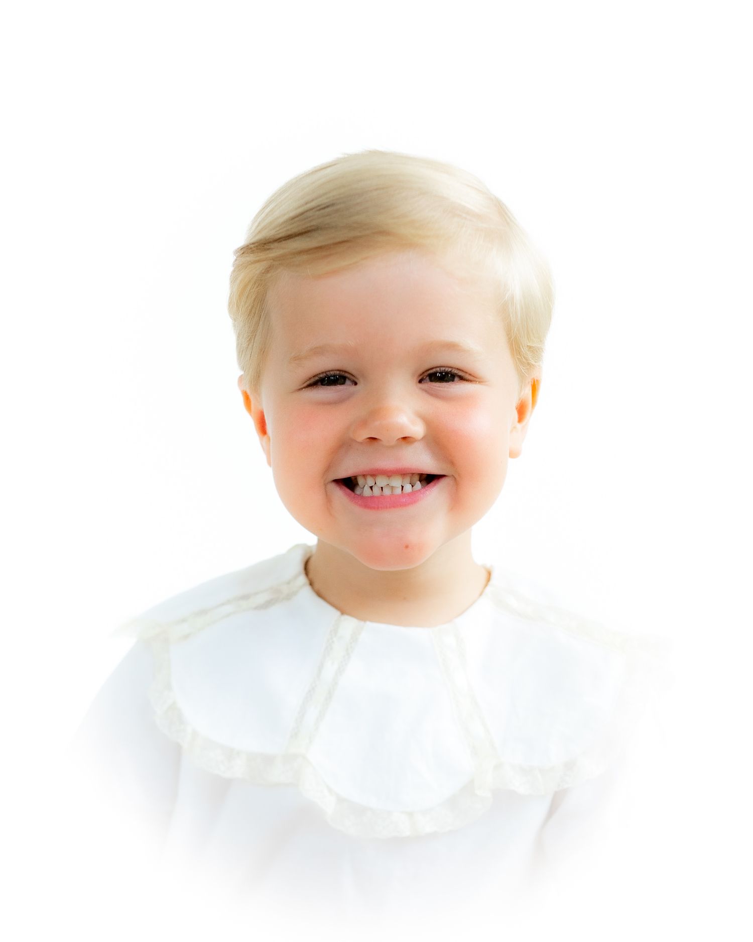 Smiling blonde toddler wearing a white ruffled collar shirt, portrait photo on white background.
