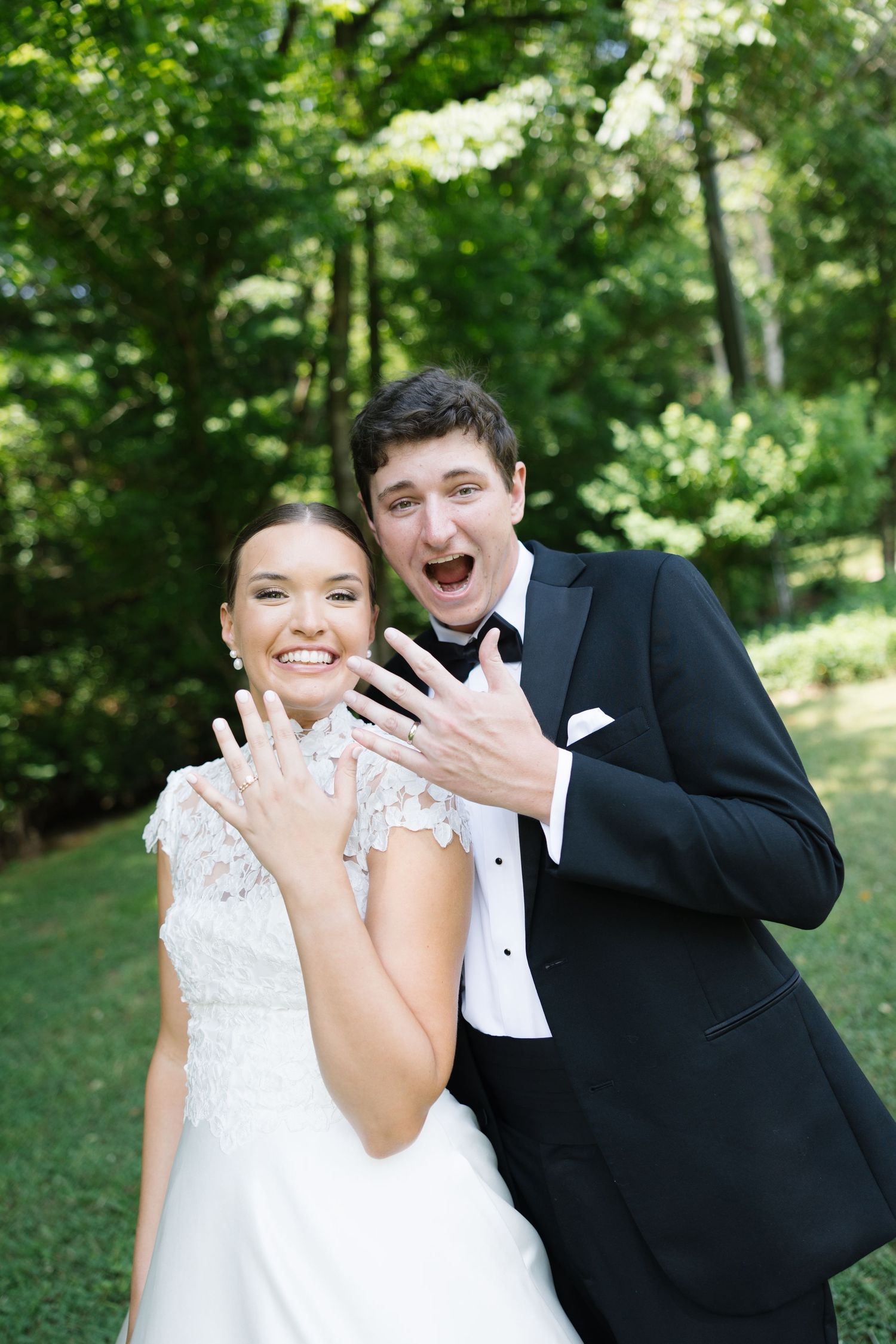Joyful newlyweds showing off wedding rings in outdoor garden setting.