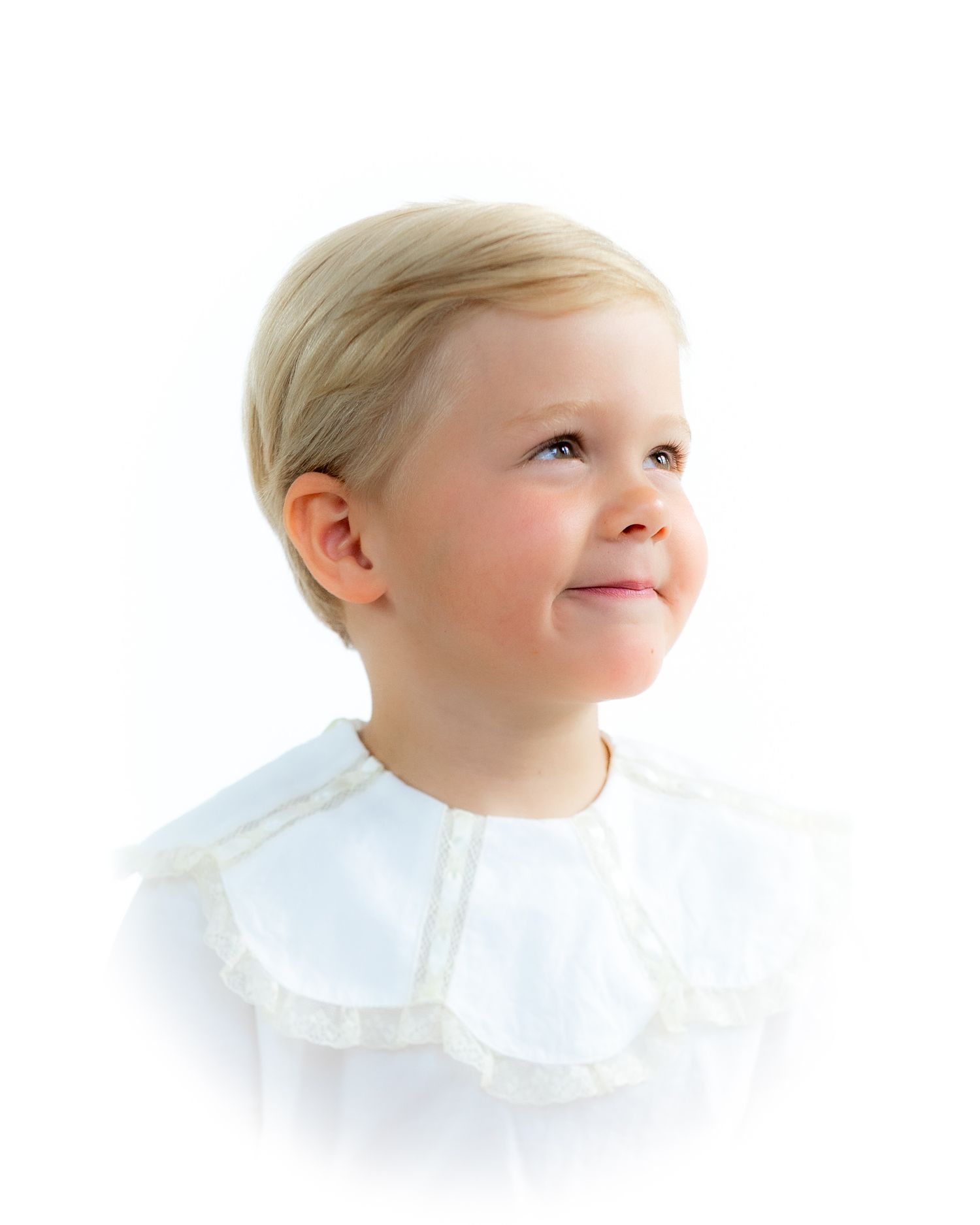 Cute blonde toddler in white lace collar shirt gazing upward, soft studio portrait.