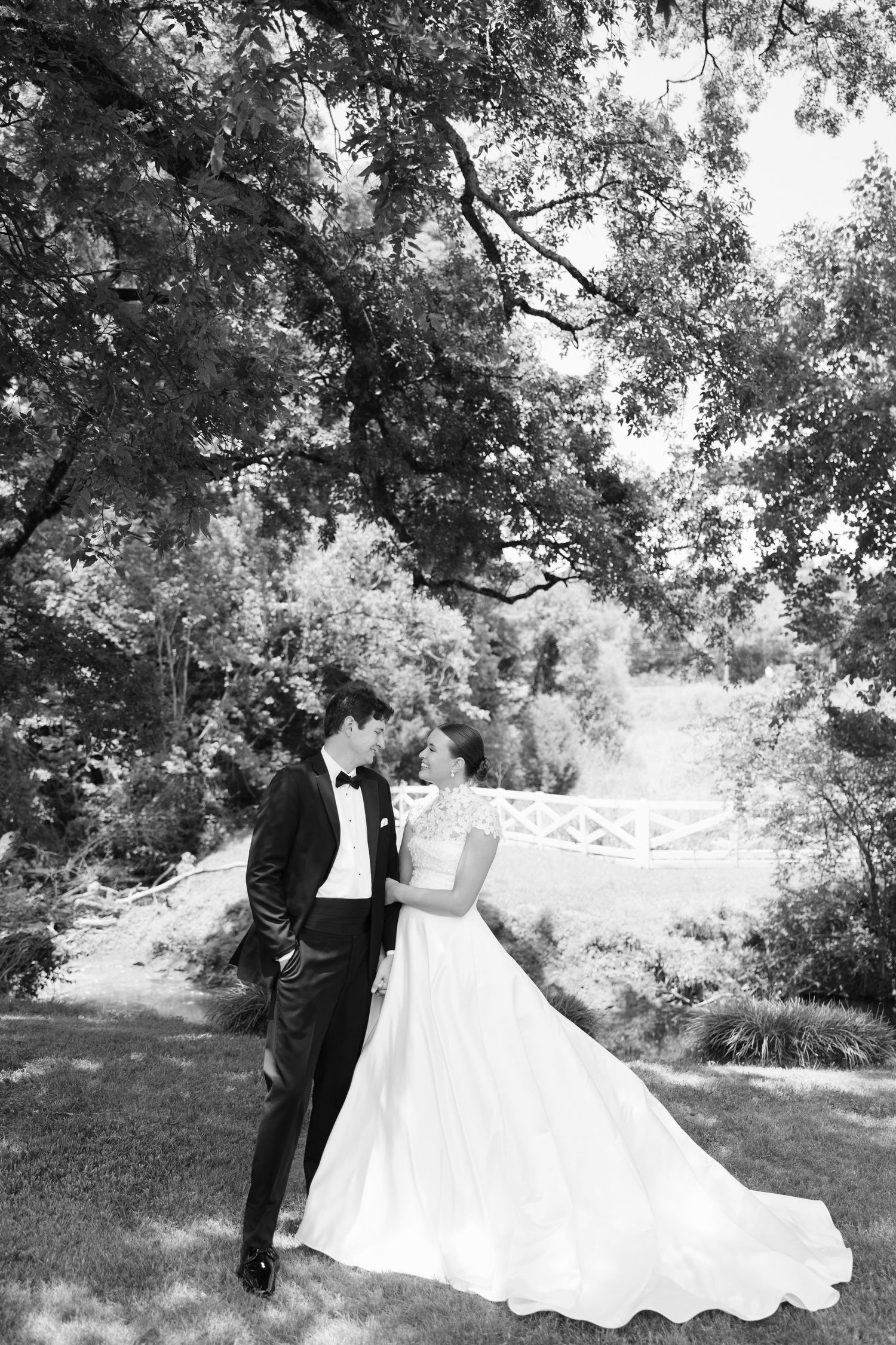 Bride and groom sharing romantic moment under large tree in black and white photo.