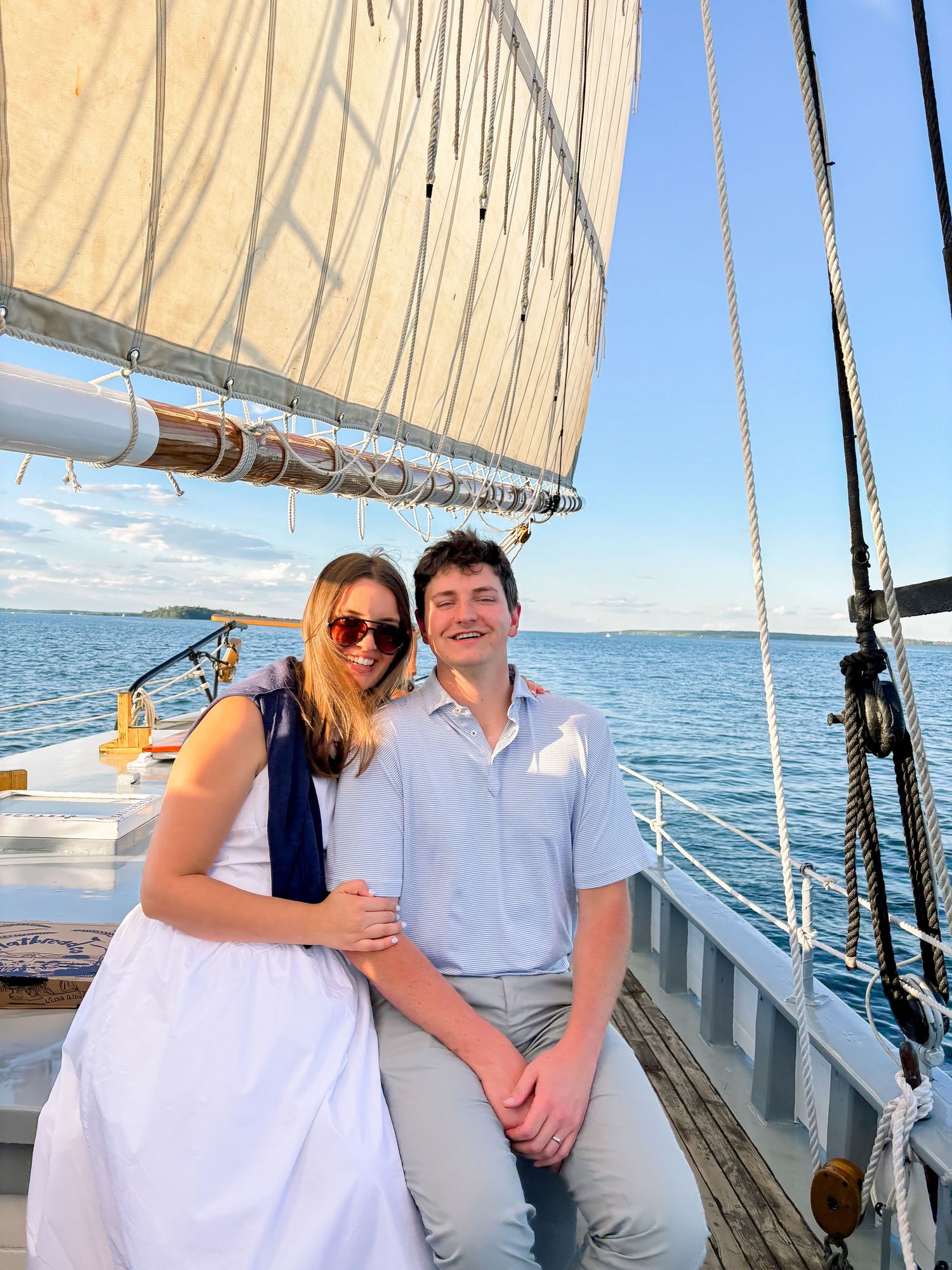 Smiling couple sitting together on a sailboat with ocean views at sunset.