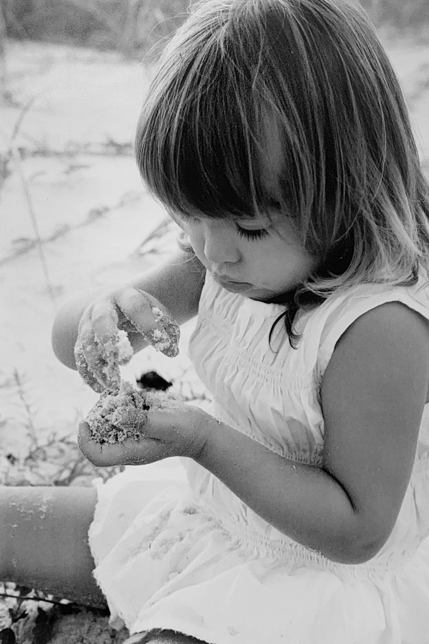 Young girl in white dress playing with sand on a beach in black and white photography.