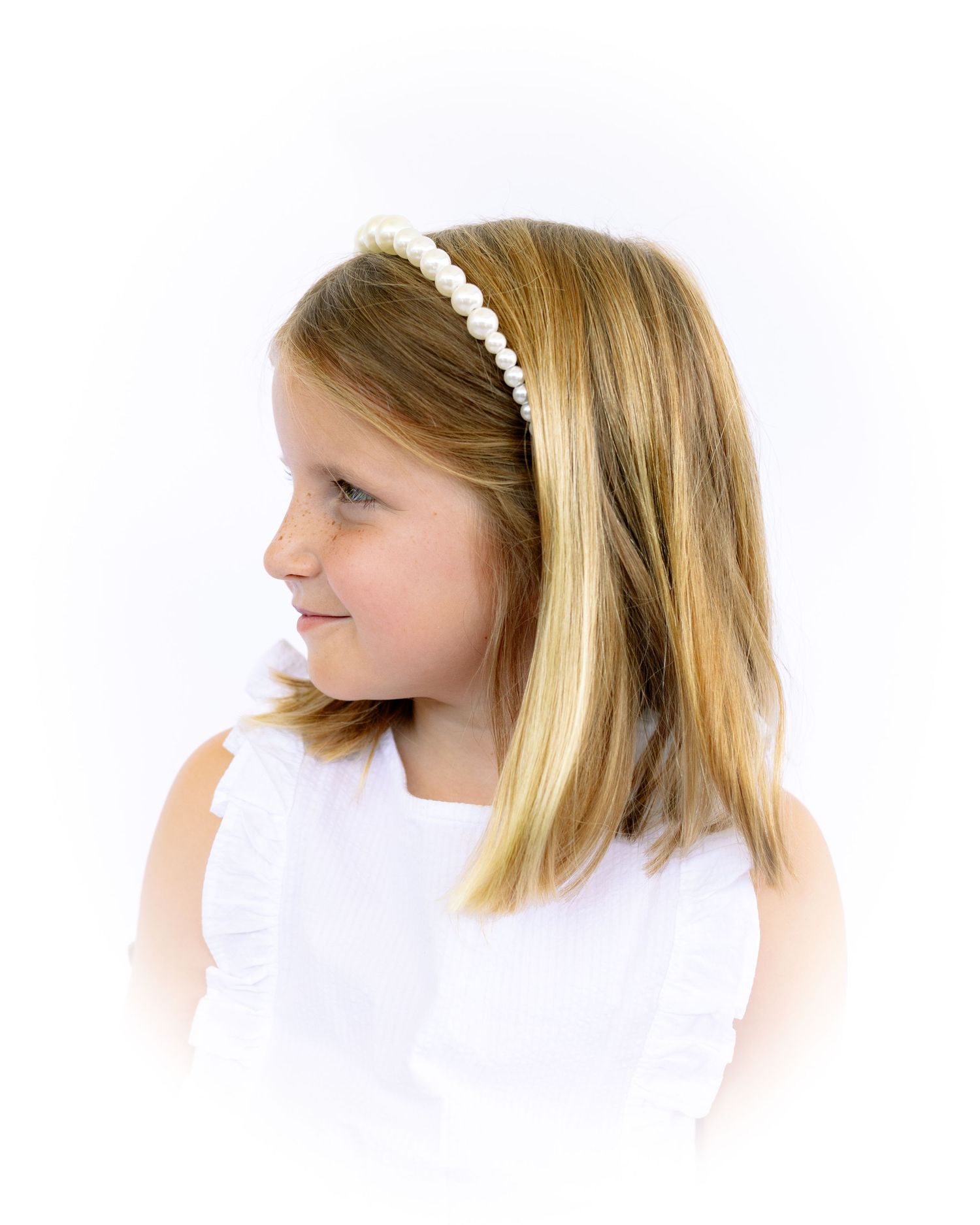 Young girl with pearl headband and blonde hair in white dress, elegant side profile portrait.