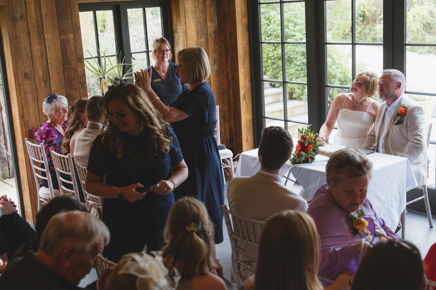 Guests mingle and celebrate at an elegant indoor wedding reception with the bride and groom seated at their table.