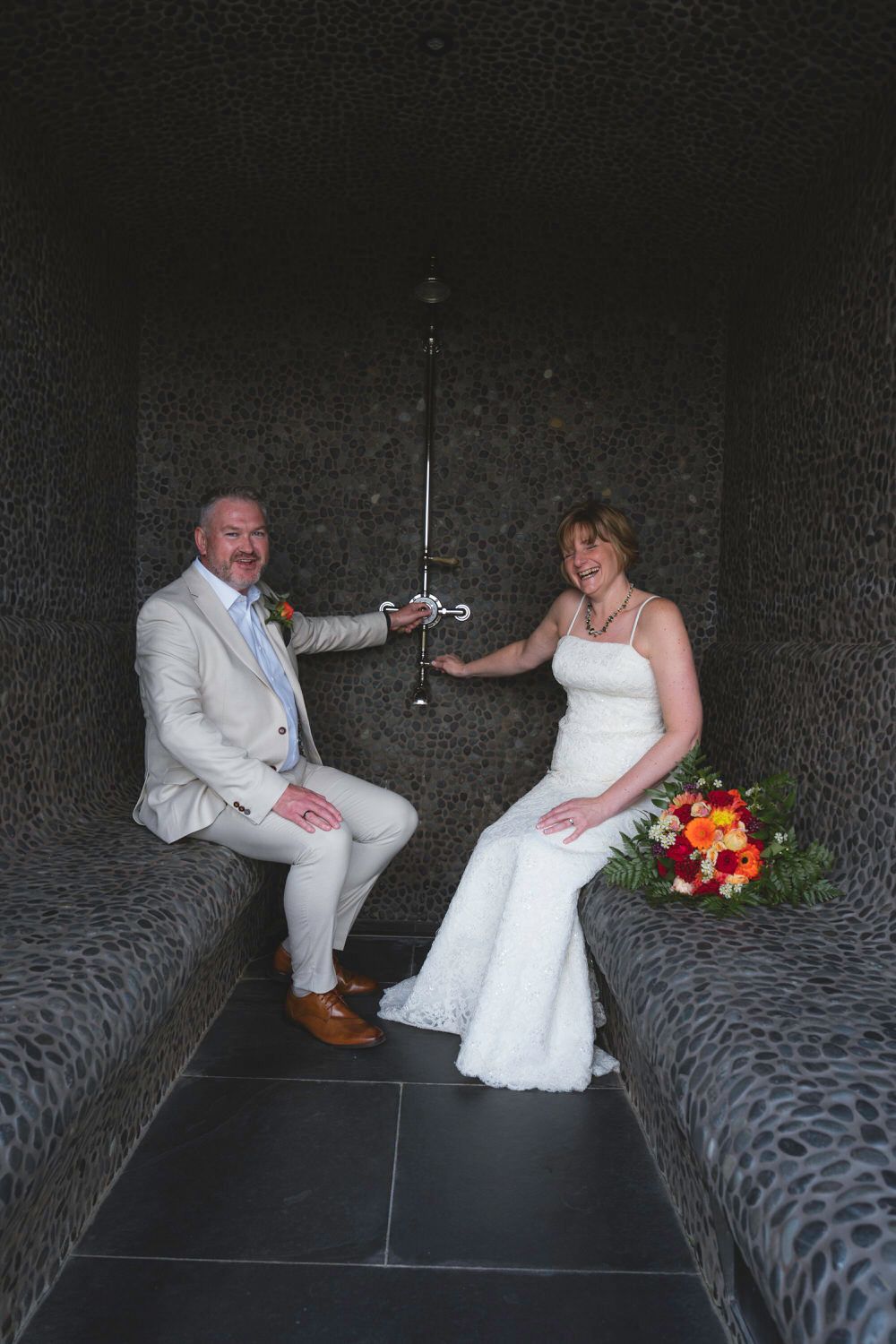 Bride and groom sit facing each other holding a sword between them in a textured stone alcove.