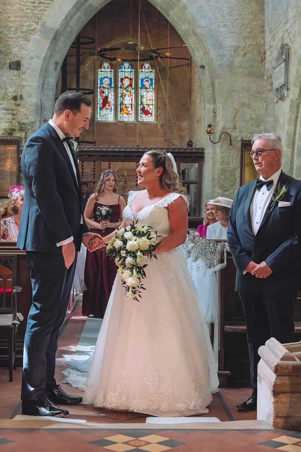 Bride and groom exchange vows at a traditional church wedding ceremony, bride holding white floral bouquet.