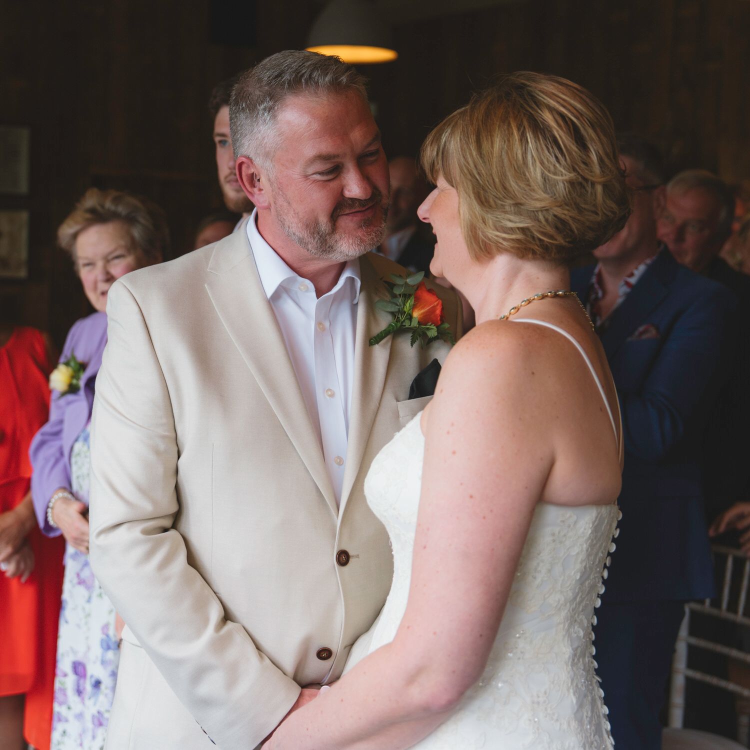 A couple shares a joyful moment during their wedding ceremony, the groom in a beige suit and bride in white dress.