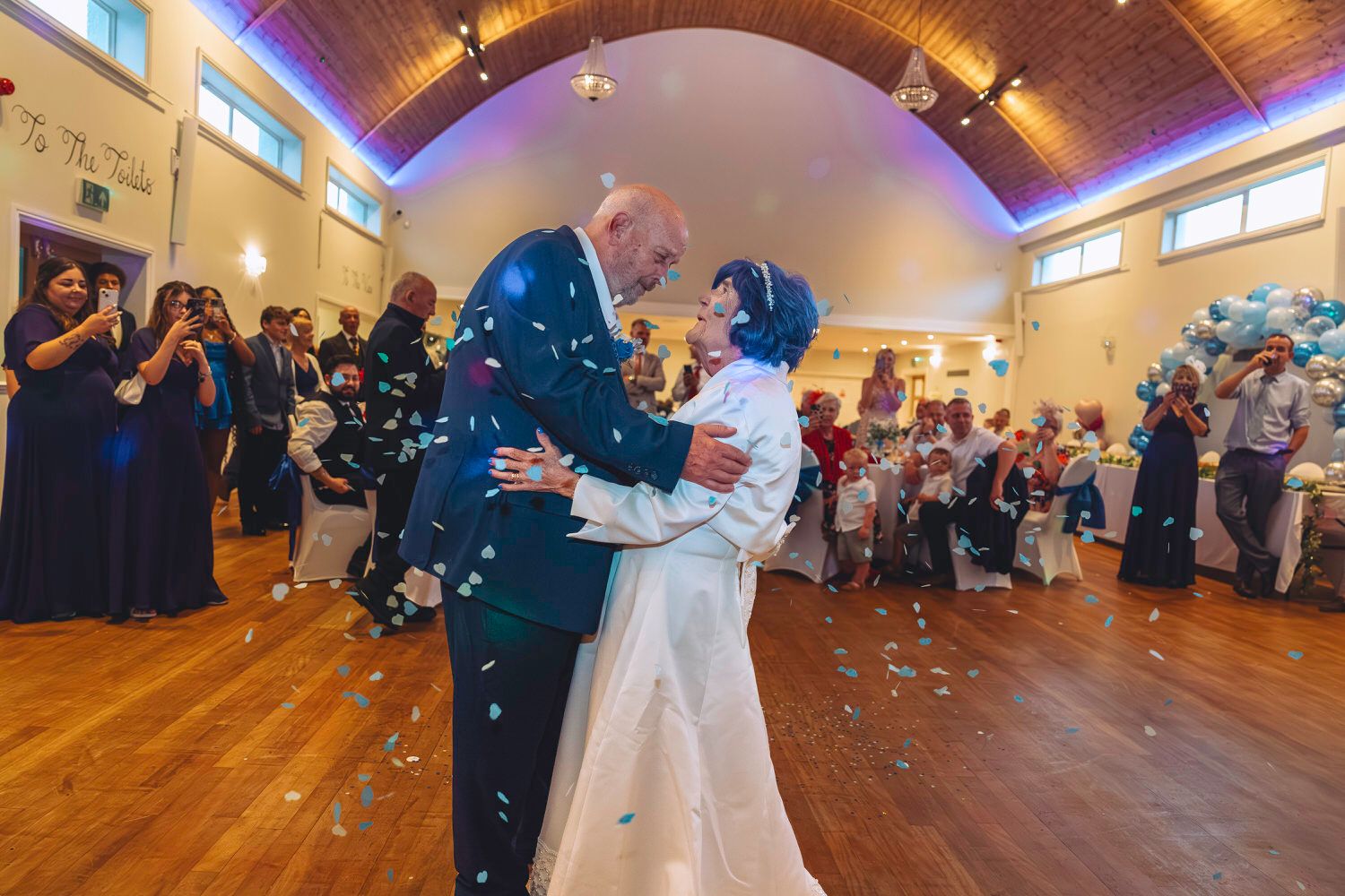 Bride and groom share first dance surrounded by colorful confetti and guests at elegant wedding reception hall.