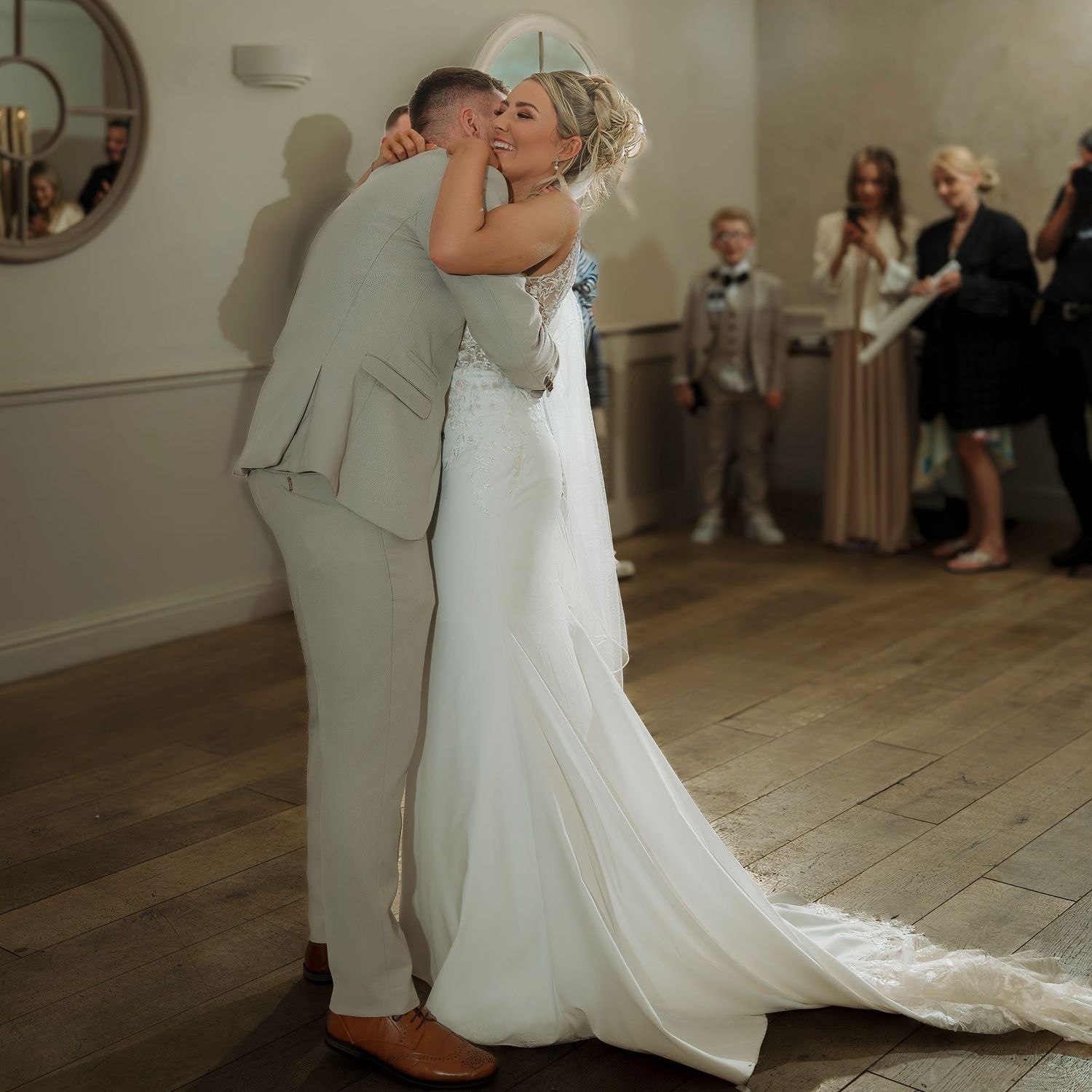 A bride and groom share their first dance, embracing tenderly in a warmly lit wedding reception venue.