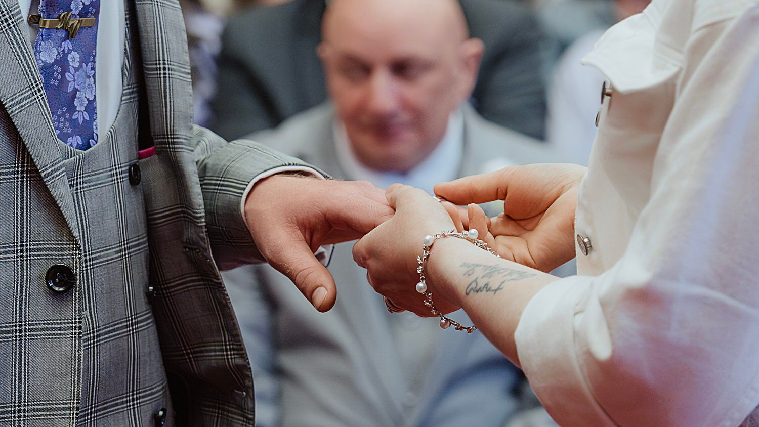 Close-up of bride placing wedding ring on grooms finger during ring exchange ceremony.