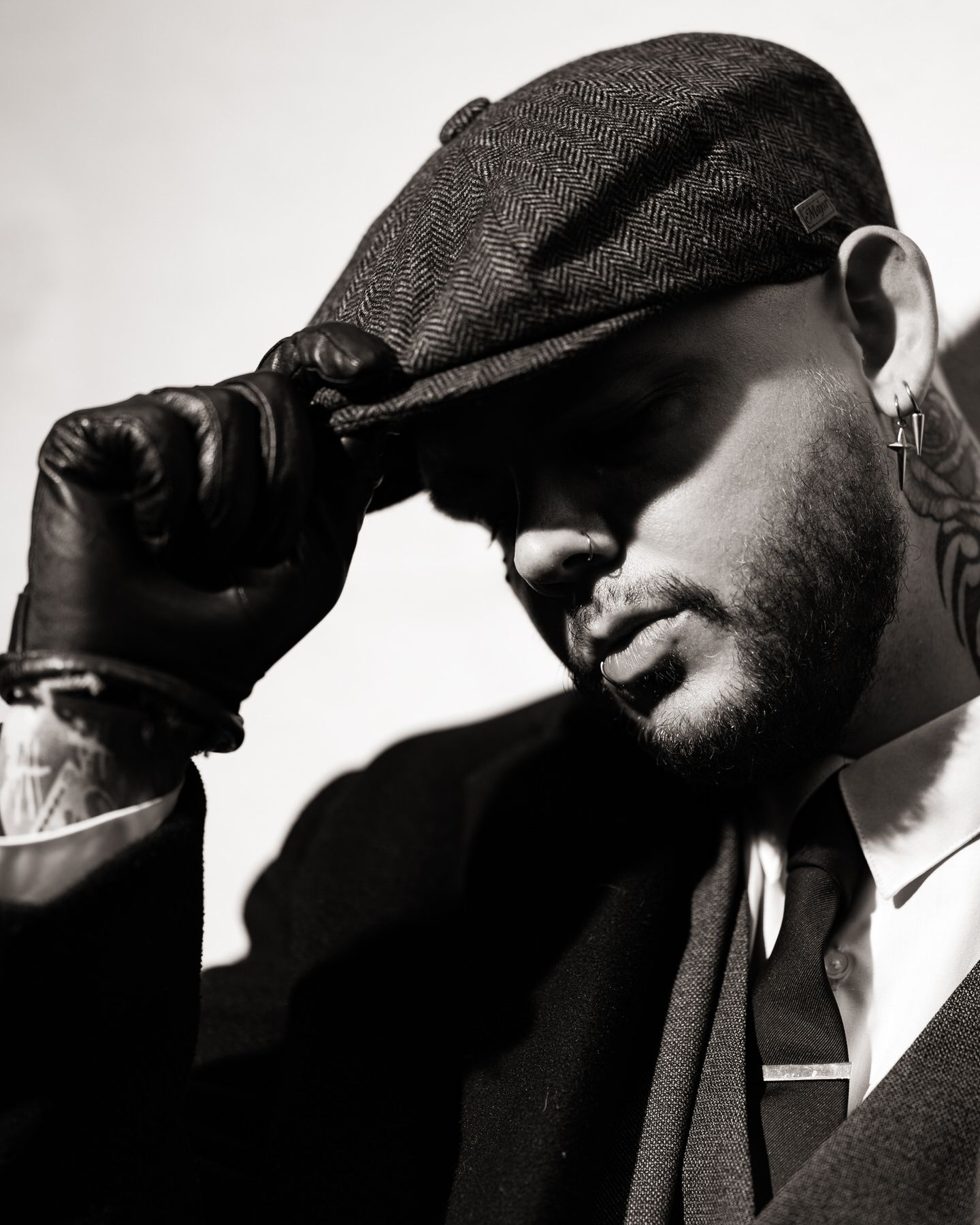 Close-up black and white portrait of man adjusting flat cap with leather glove.