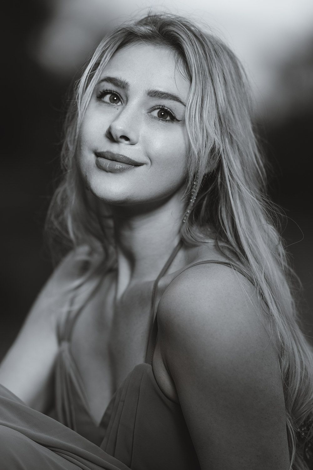 Black and white portrait of a smiling blonde woman with long hair wearing a spaghetti strap dress.