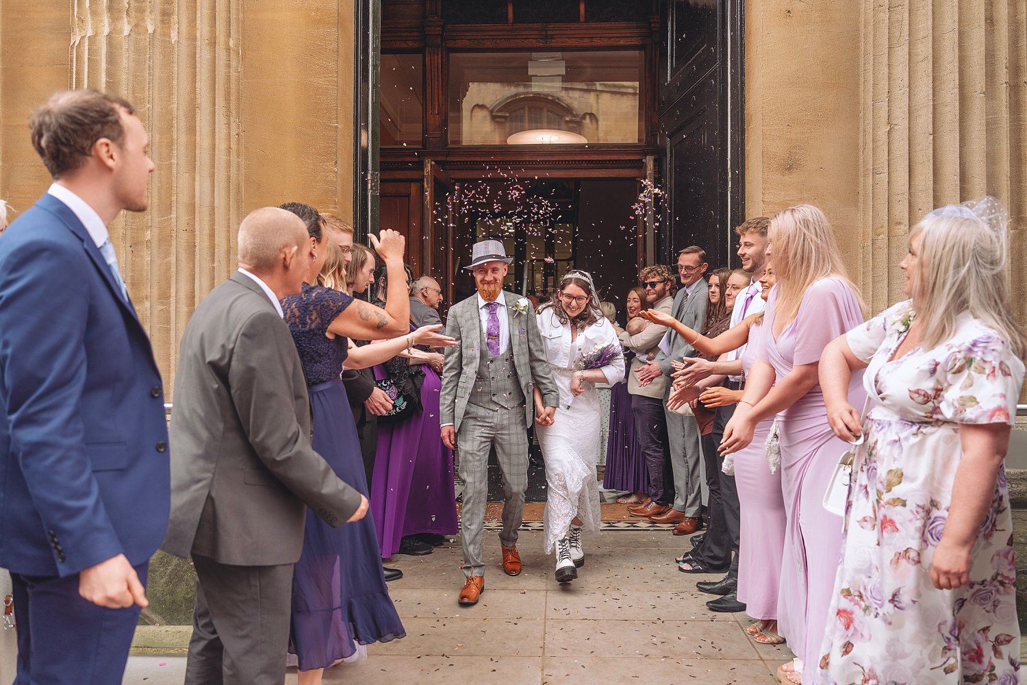 Newlywed couple exits church ceremony as guests celebrate with confetti in a joyful outdoor wedding.