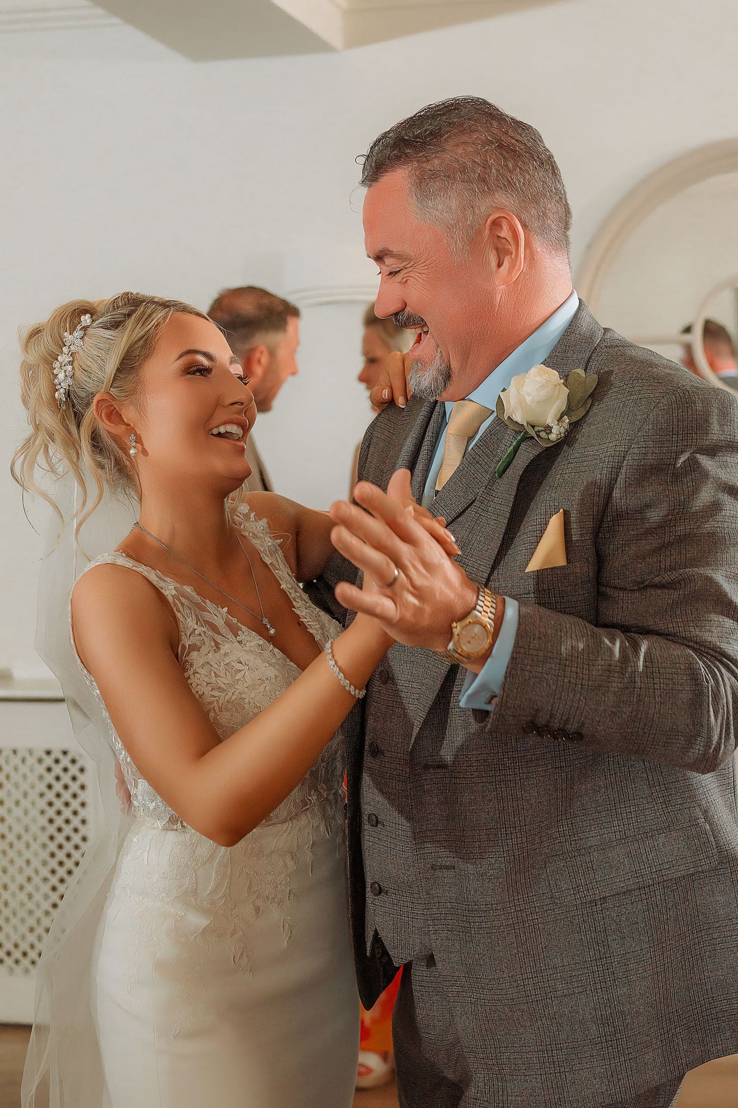 Bride and groom share a joyful moment during their wedding reception, with the groom wearing a grey suit and blue tie.