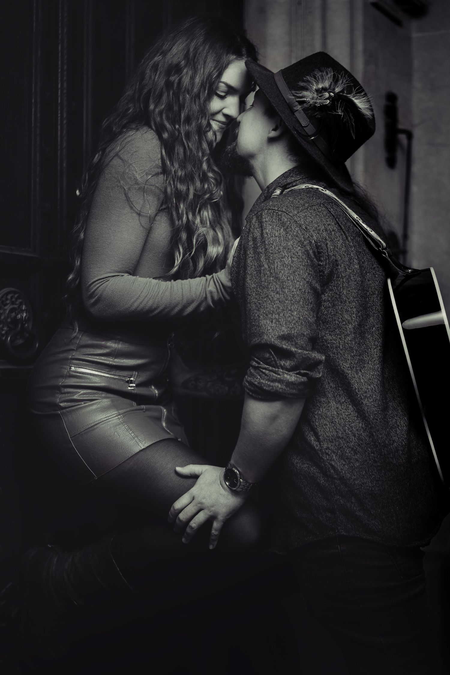 Black and white photo of a romantic couple sharing an intimate moment, a hat-wearing guitarist leaning in to kiss a smiling woman.
