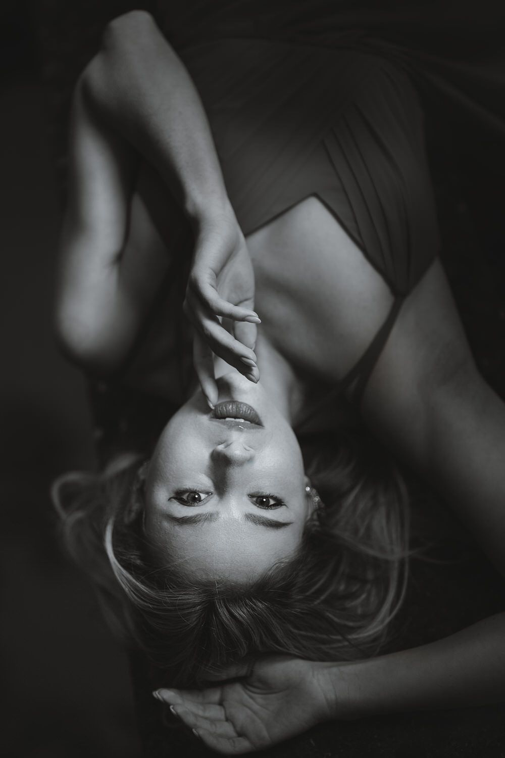 Black and white portrait of a woman lying back with hands near face, dramatic lighting, artistic photography.