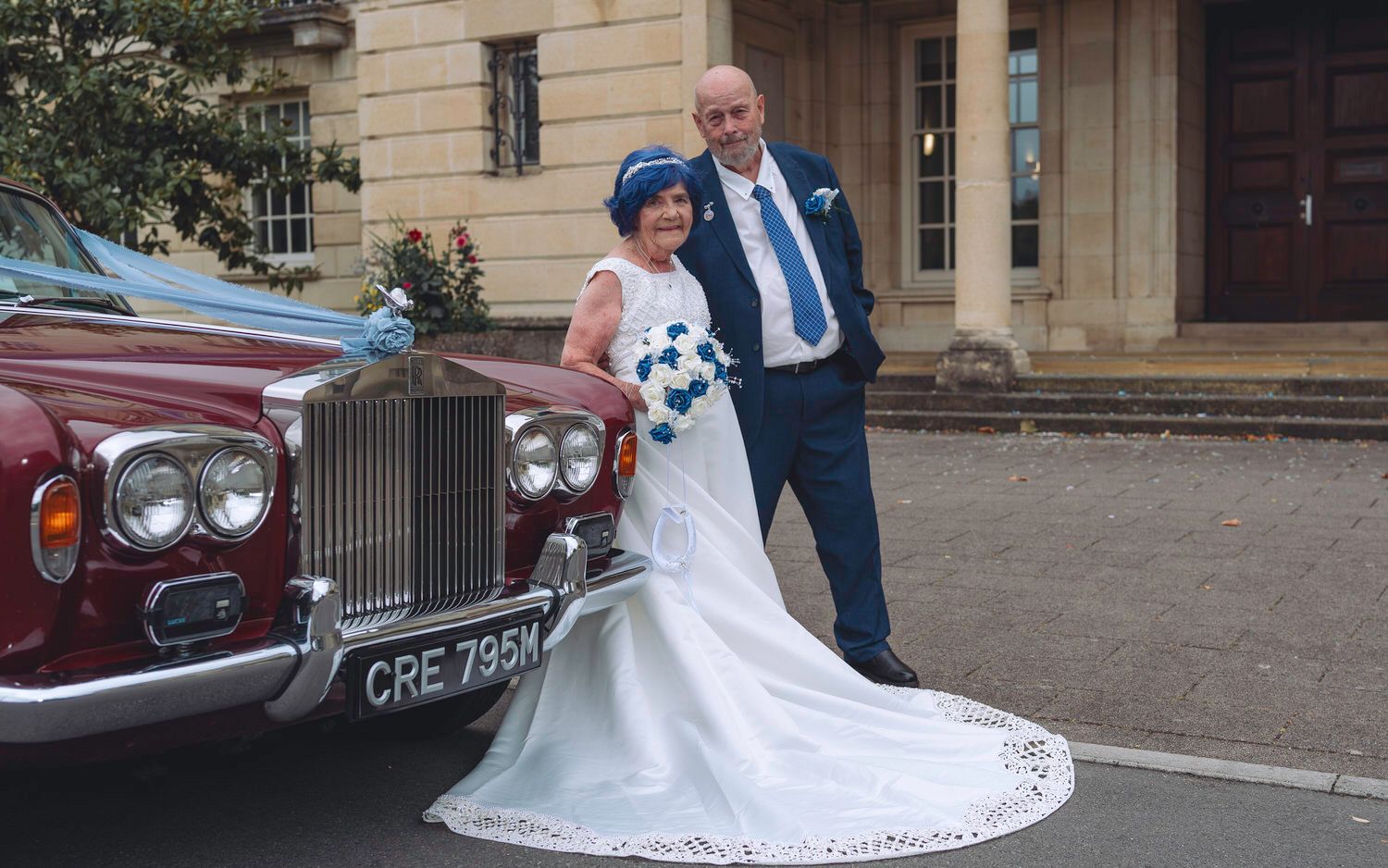Bride and groom posing beside a vintage Rolls-Royce at their wedding venue.