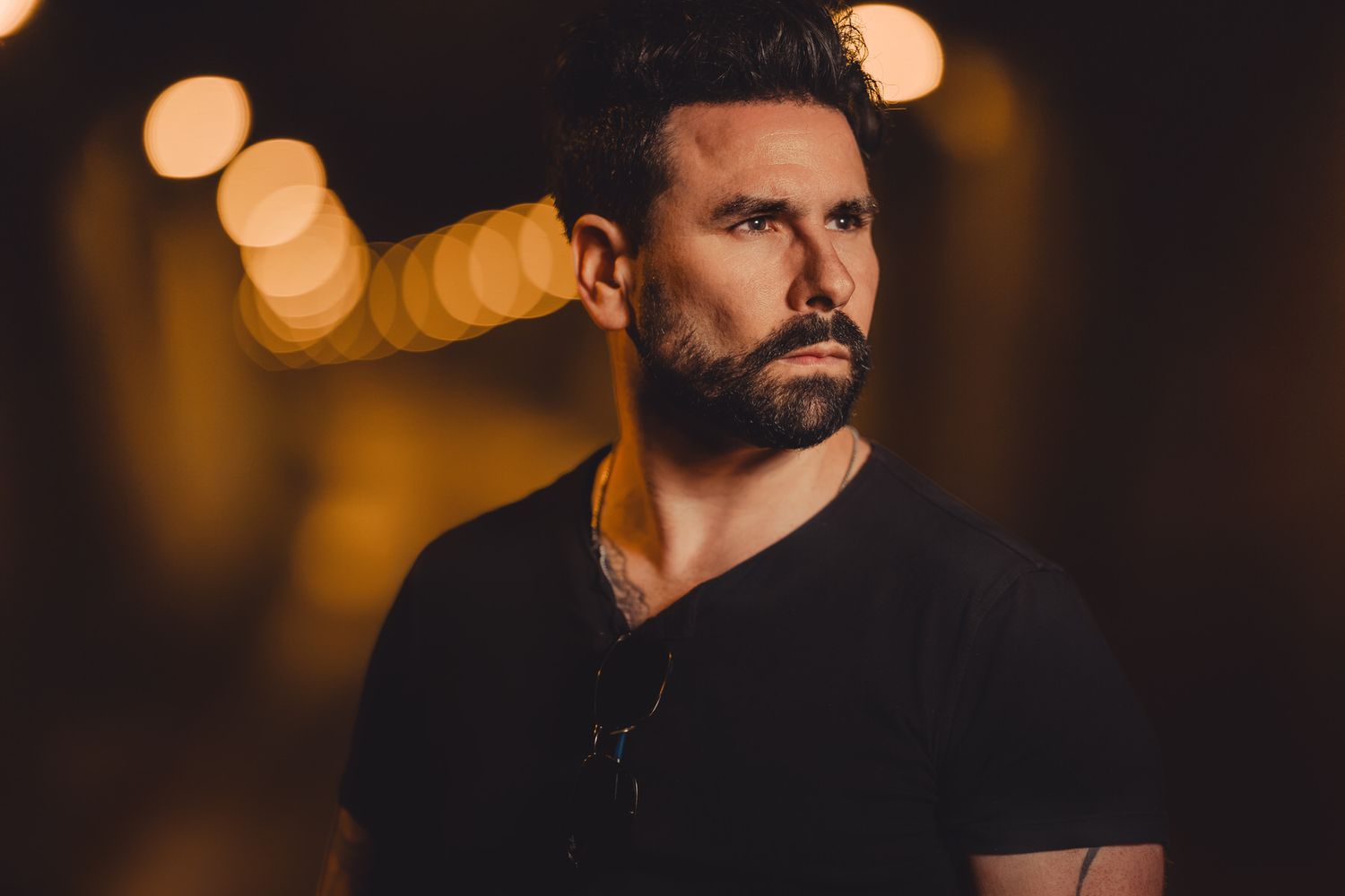 Handsome bearded man in black t-shirt with moody bokeh light background portrait.