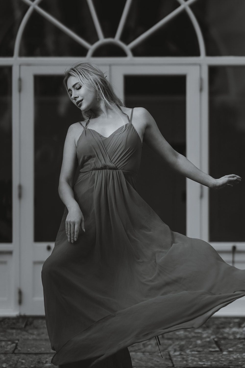 Black and white photo of a blonde woman in a flowing maxi dress dancing gracefully in front of elegant white doors.