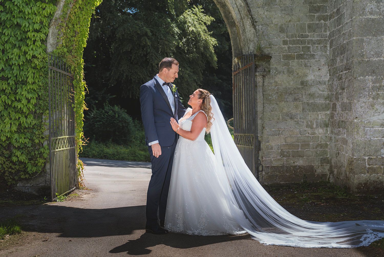 Bride and groom share a romantic moment under a stone arch surrounded by ivy on their wedding day.