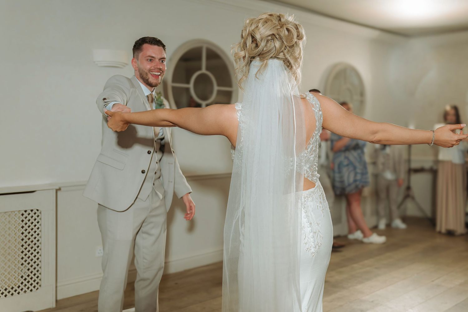 Bride and groom share a joyful first dance at their wedding reception in an elegant white venue.