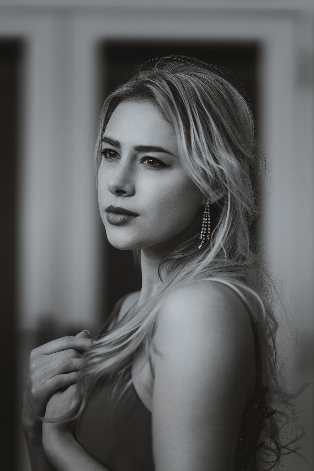 Black and white portrait of a young blonde woman with dangling earrings, gazing softly at the camera.