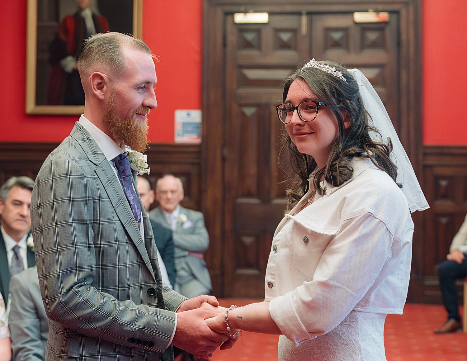Bride and groom exchanging rings at a civil wedding ceremony in an elegant red-walled venue.