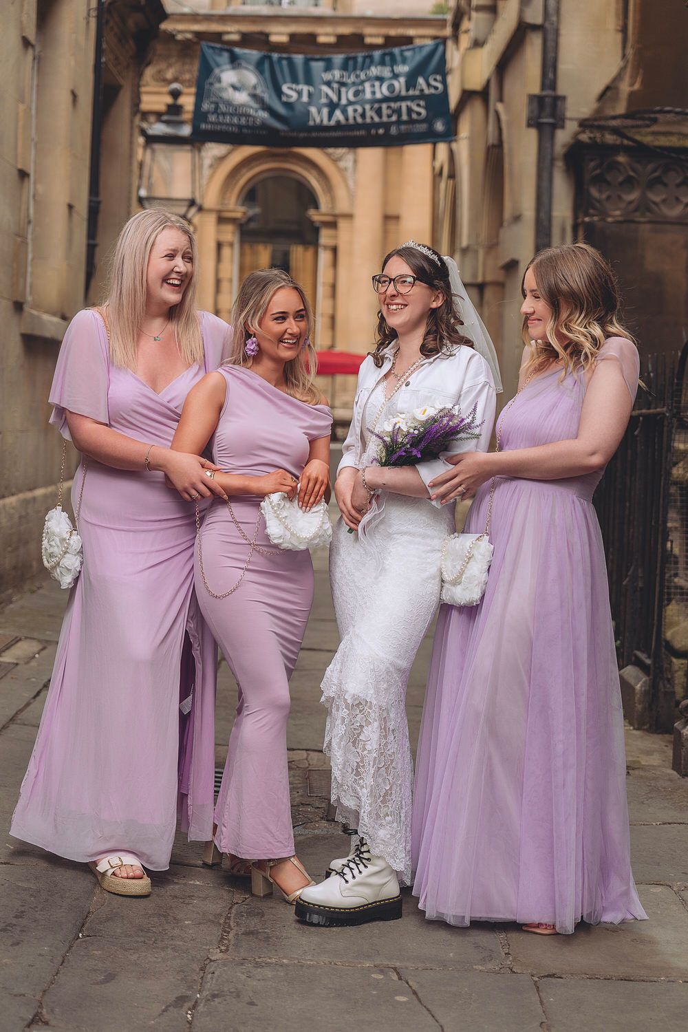 Bride in white dress with three bridesmaids in lavender gowns outside St Nicholas Markets.