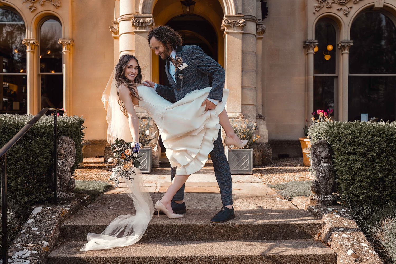 Bride and groom posing on stone steps outside a grand Gothic-style wedding venue.