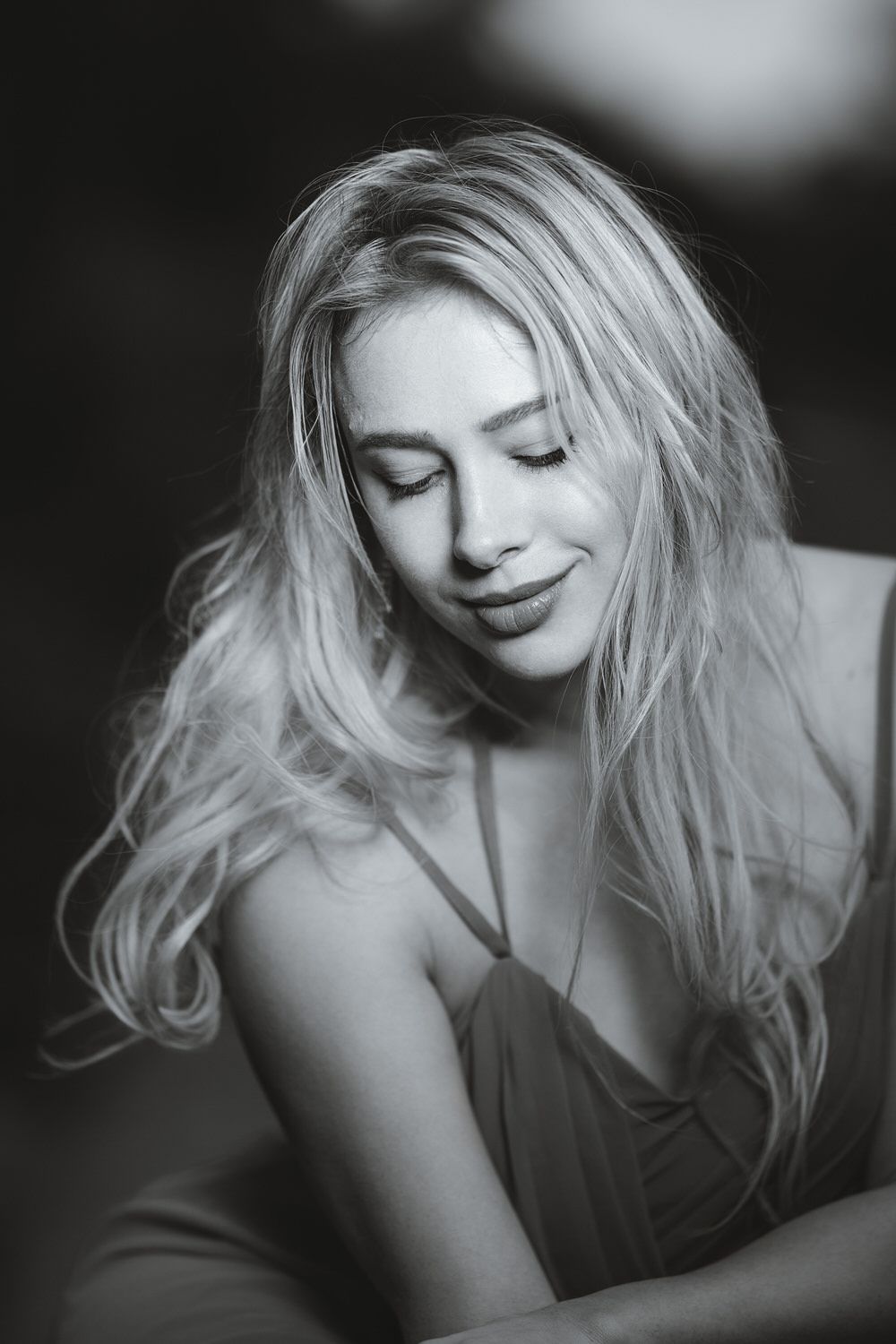 Black and white portrait of a smiling blonde woman with long hair, eyes closed, wearing a spaghetti strap dress.
