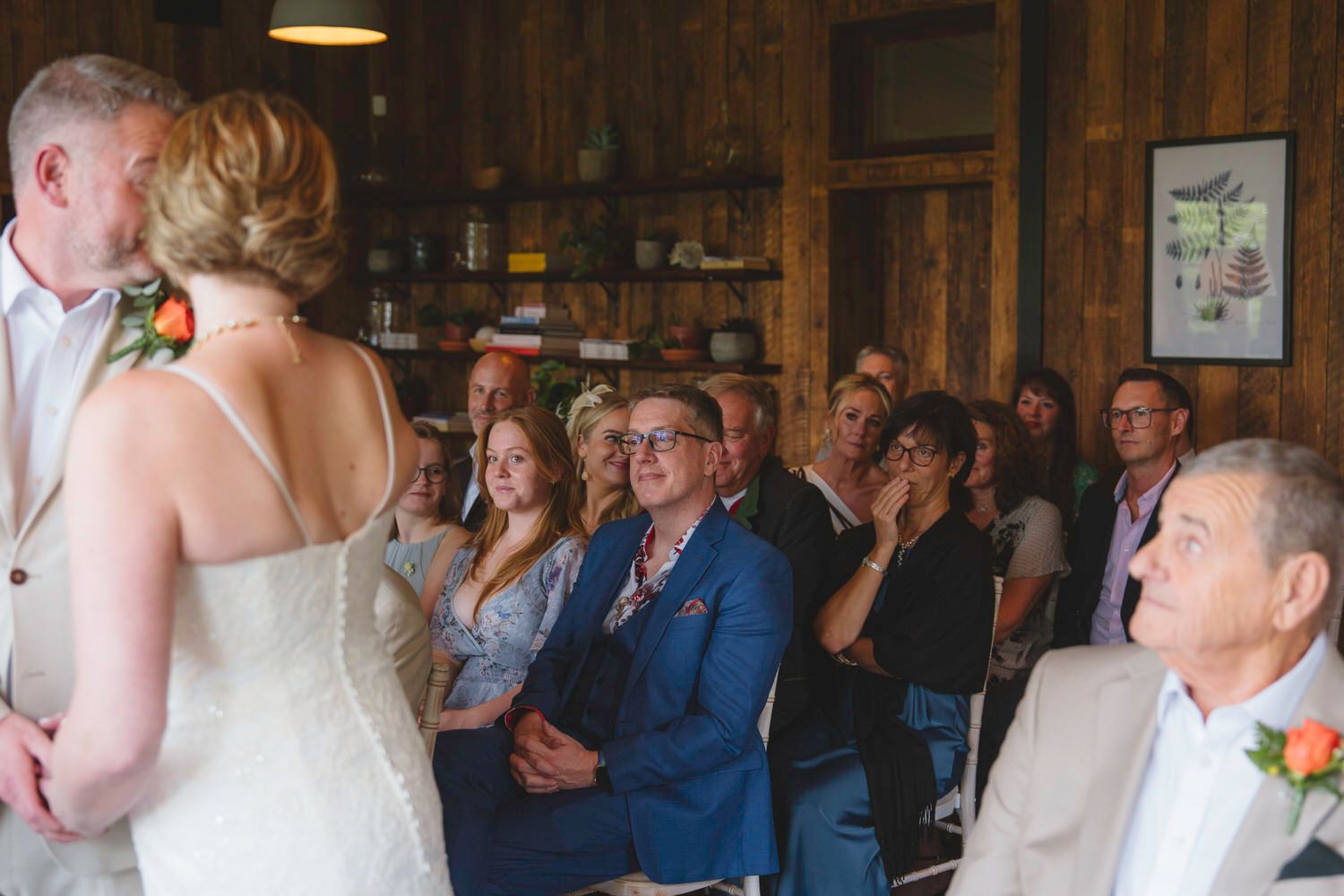 Wedding guests smile and applaud during an intimate rustic barn ceremony as the bride stands before the audience.
