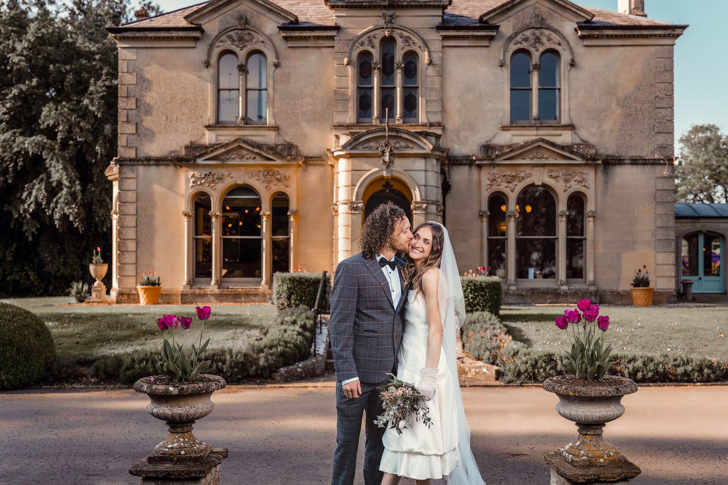 Bride and groom posing romantically at dusk in front of an elegant Gothic manor wedding venue.
