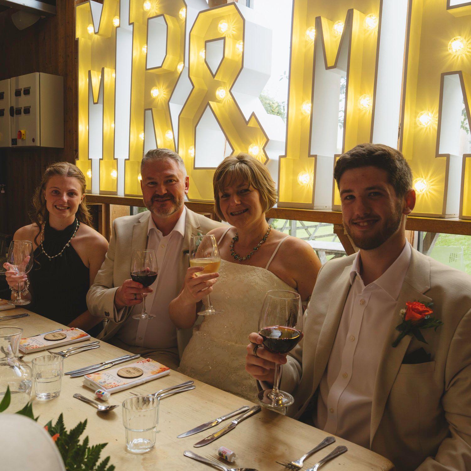 Wedding party of four guests toasting with wine glasses in front of a decorative Mr & Mrs marquee sign.