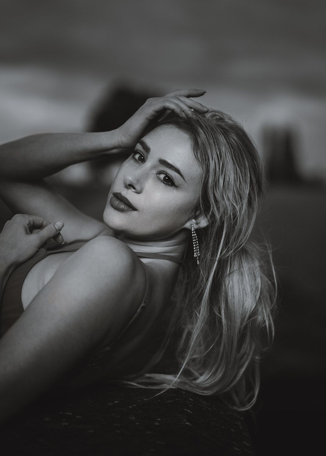 Black and white portrait of a blonde woman with dangling earrings posing elegantly with hand in hair.