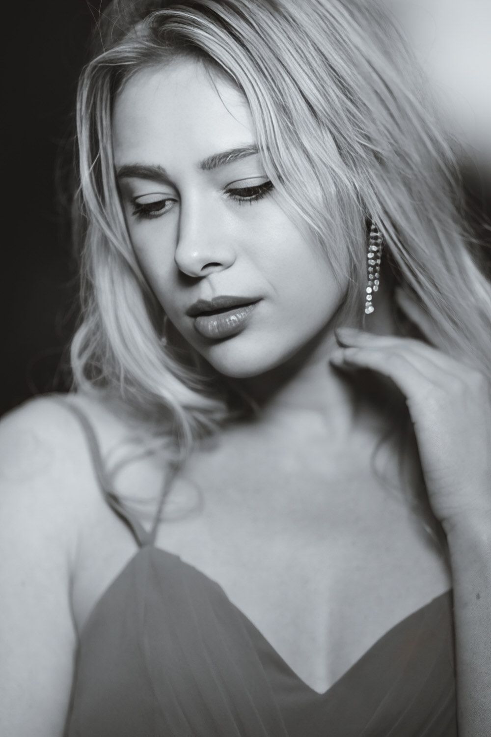 Black and white portrait of a blonde woman in a dress wearing dangling earrings, looking down elegantly.