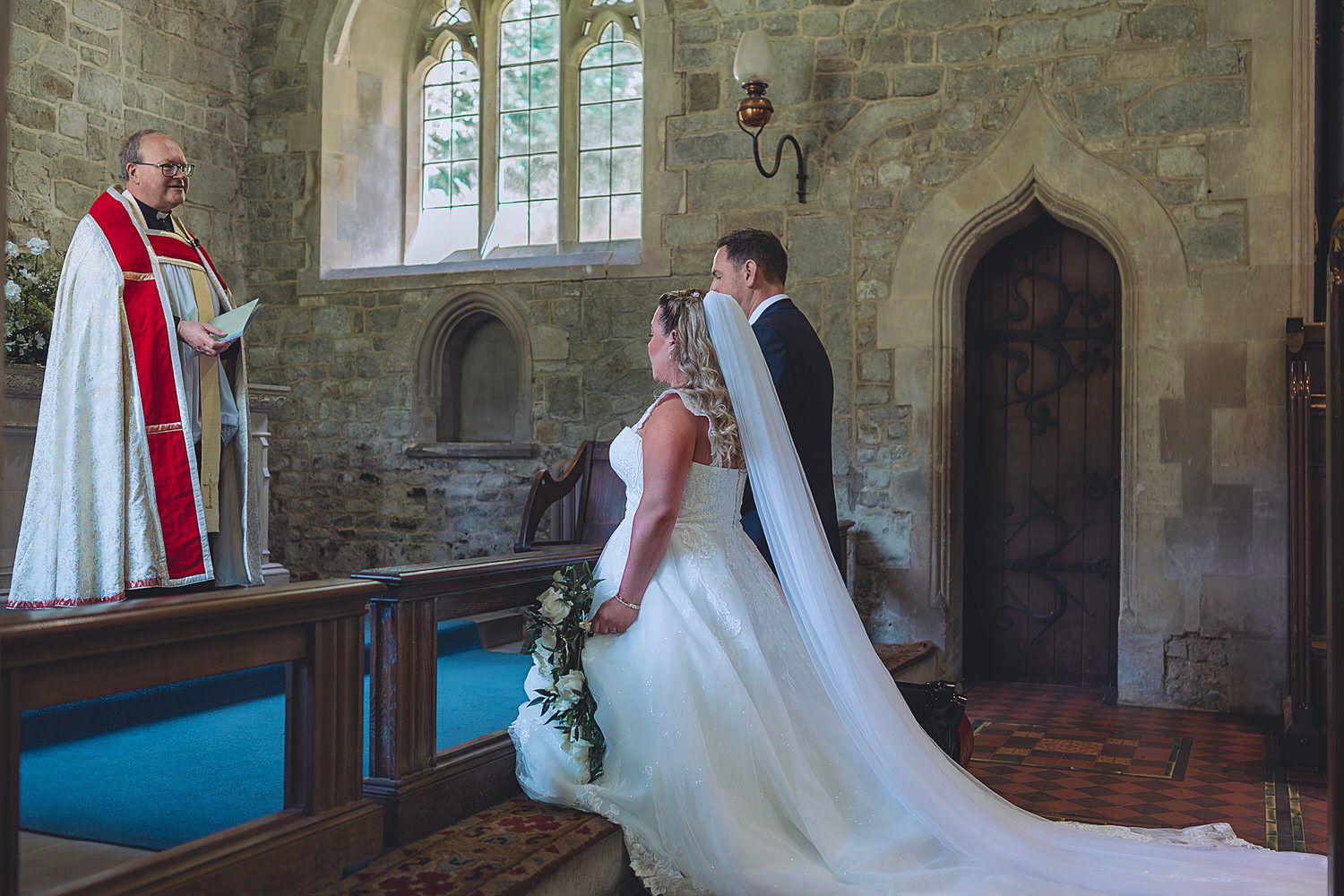 A bride and groom exchange vows before a robed officiant in a historic stone church wedding ceremony.