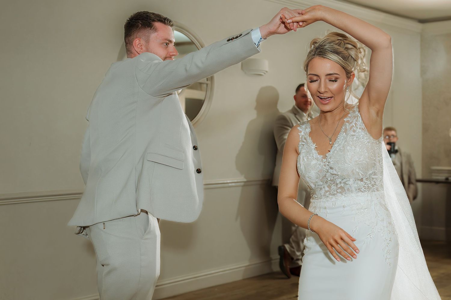 Bride and groom share a joyful first dance, with groom spinning bride in elegant white wedding gown and beaded belt.