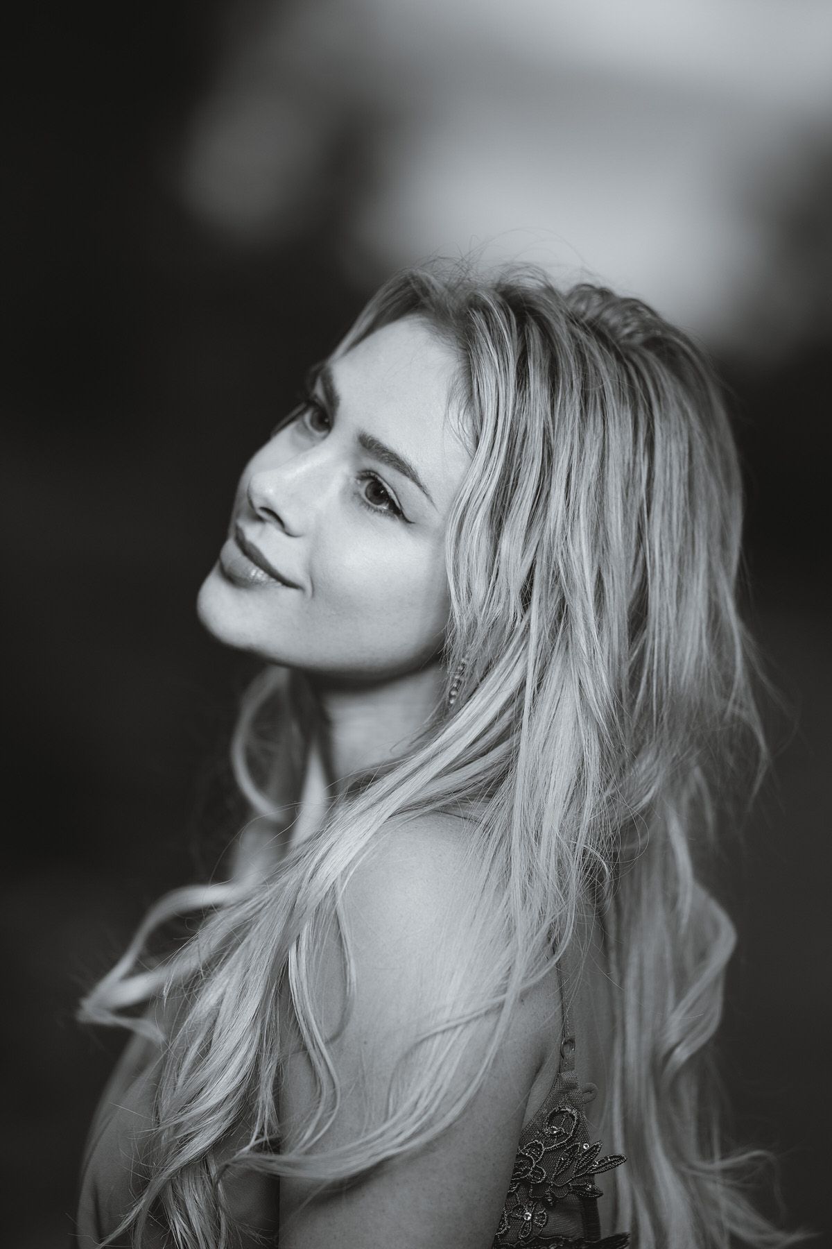 Black and white portrait of a smiling blonde woman with flowing hair outdoors.